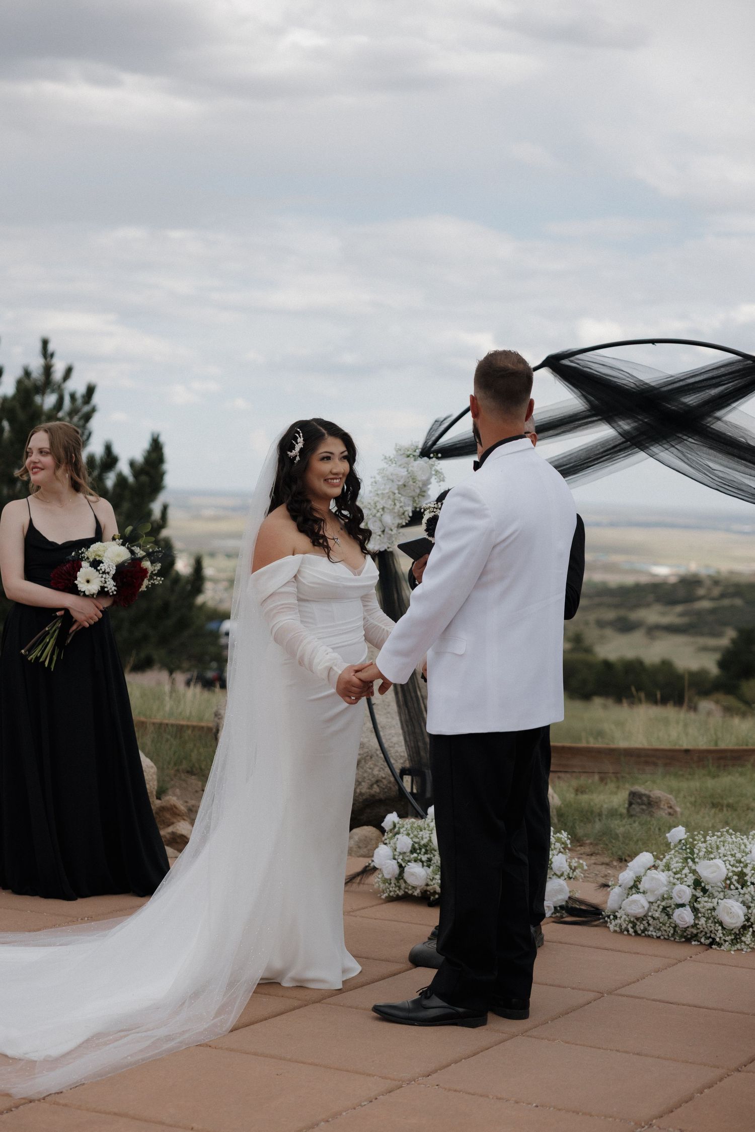 Bride and groom exchange vows outdoors at scenic hilltop wedding ceremony with black and white decor.