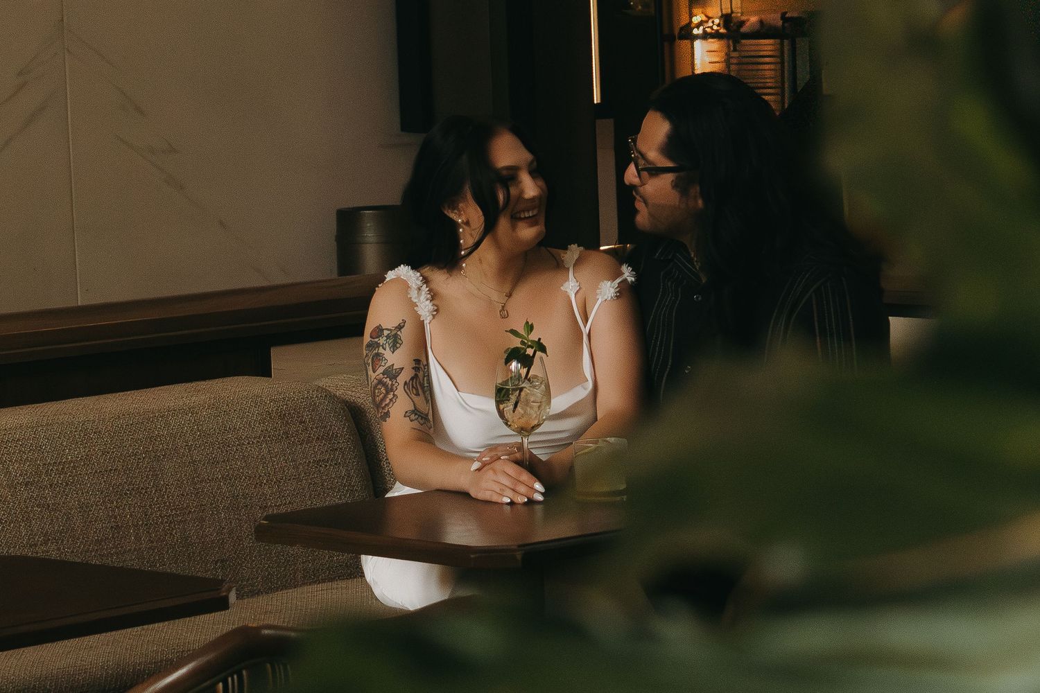 Bride and groom seated at a table in an intimate restaurant setting with warm lighting and wine glasses.