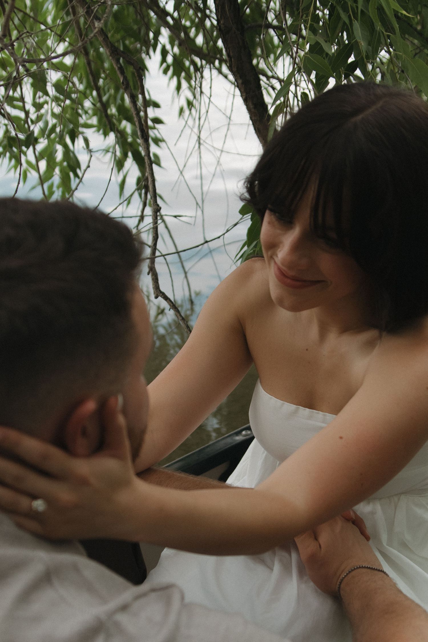 A tender embrace captured between two people with willow tree branches in the foreground.