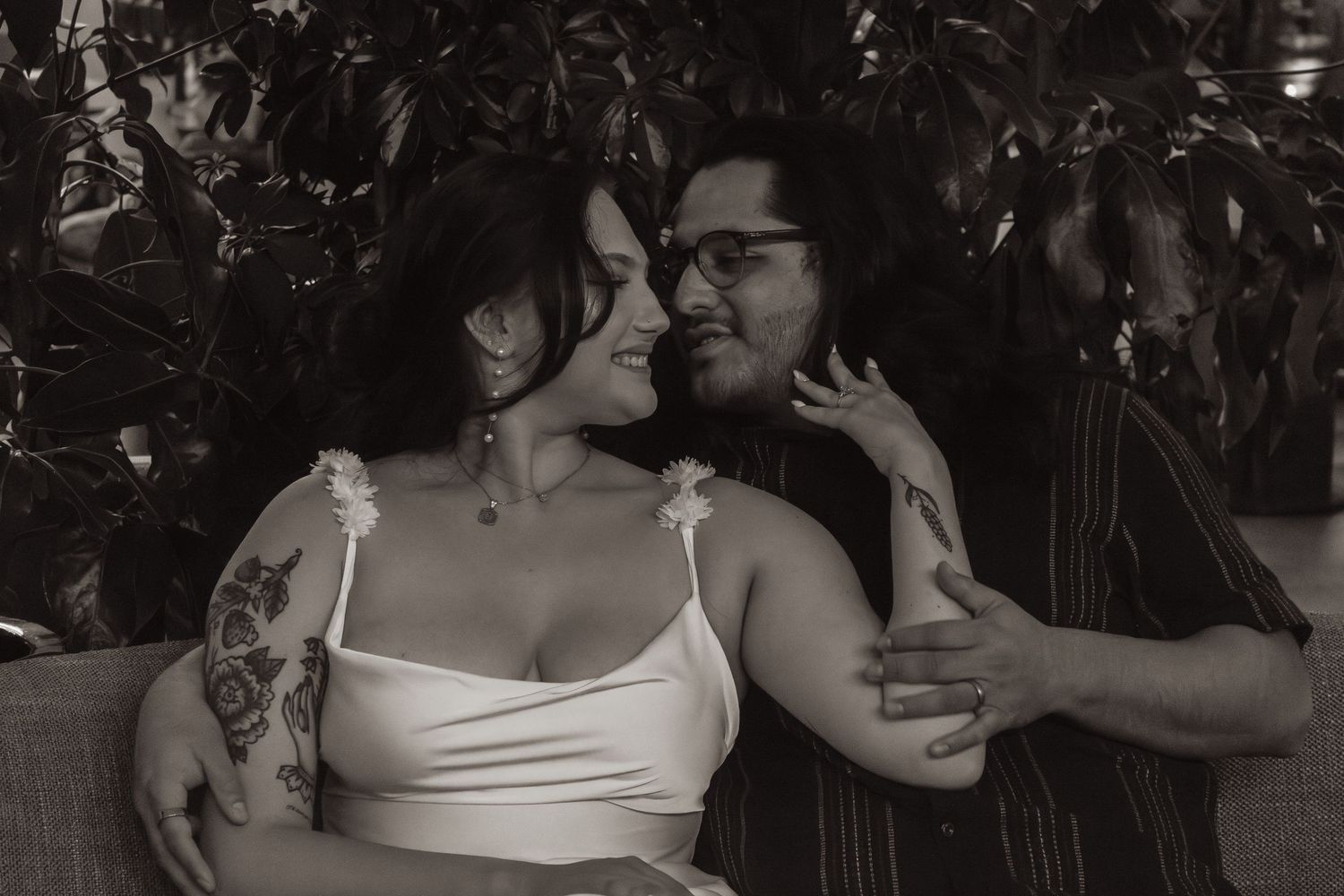An intimate moment captured in black and white with soft lighting and greenery in the background.