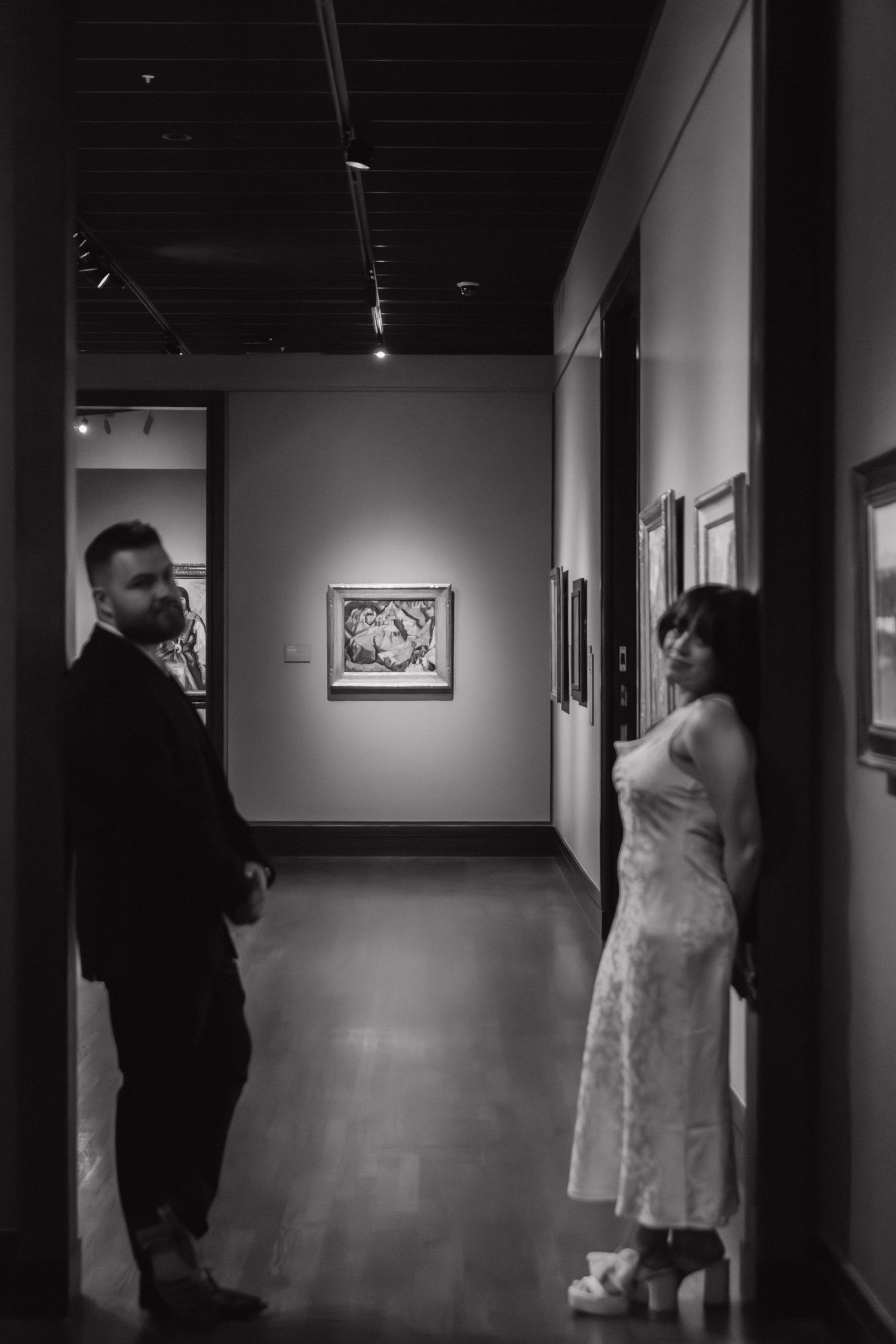 Black and white gallery sequence showing people viewing artwork in a dimly lit hallway.
