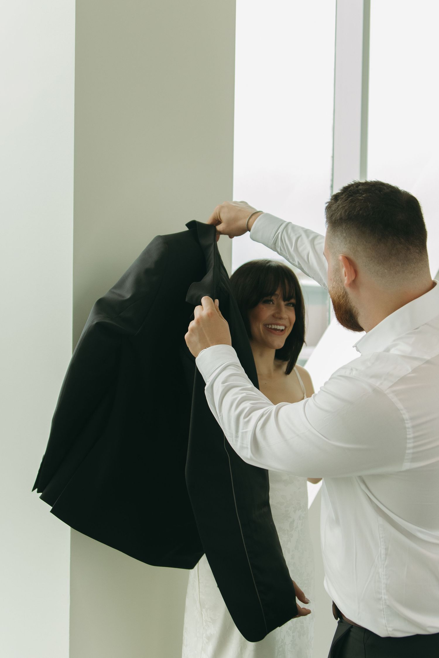 A couple in black and white clothing interacts playfully against a minimalist white backdrop.