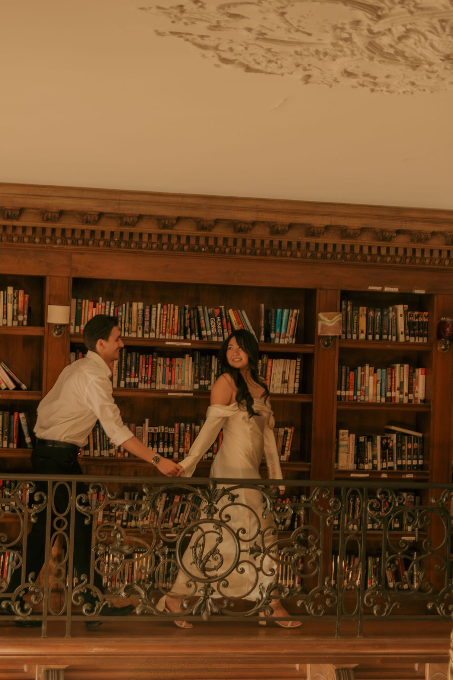Couple sitting together on an ornate balcony railing in a vintage library.