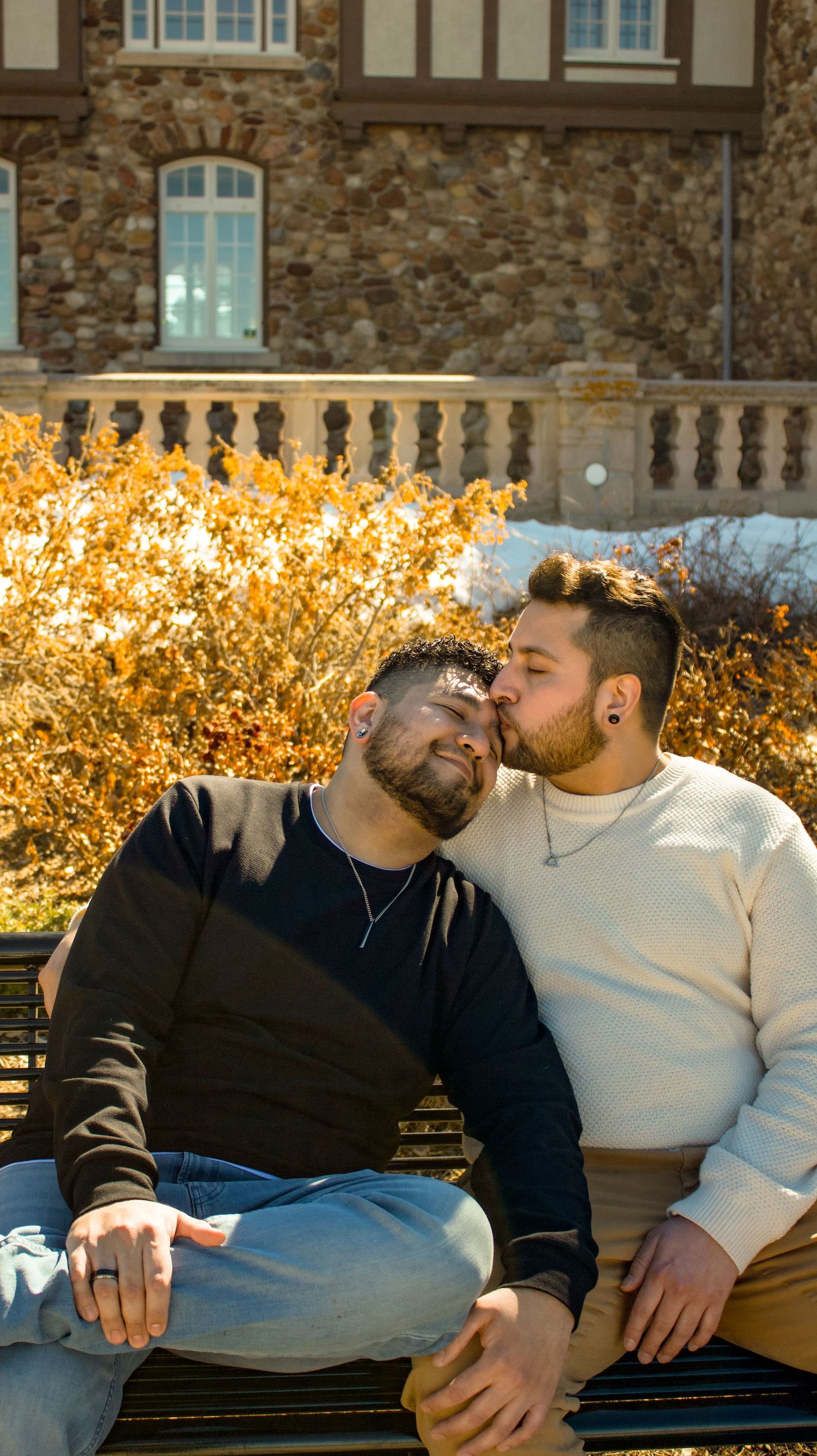 Two people sharing intimate moment on bench with stone architecture in background.