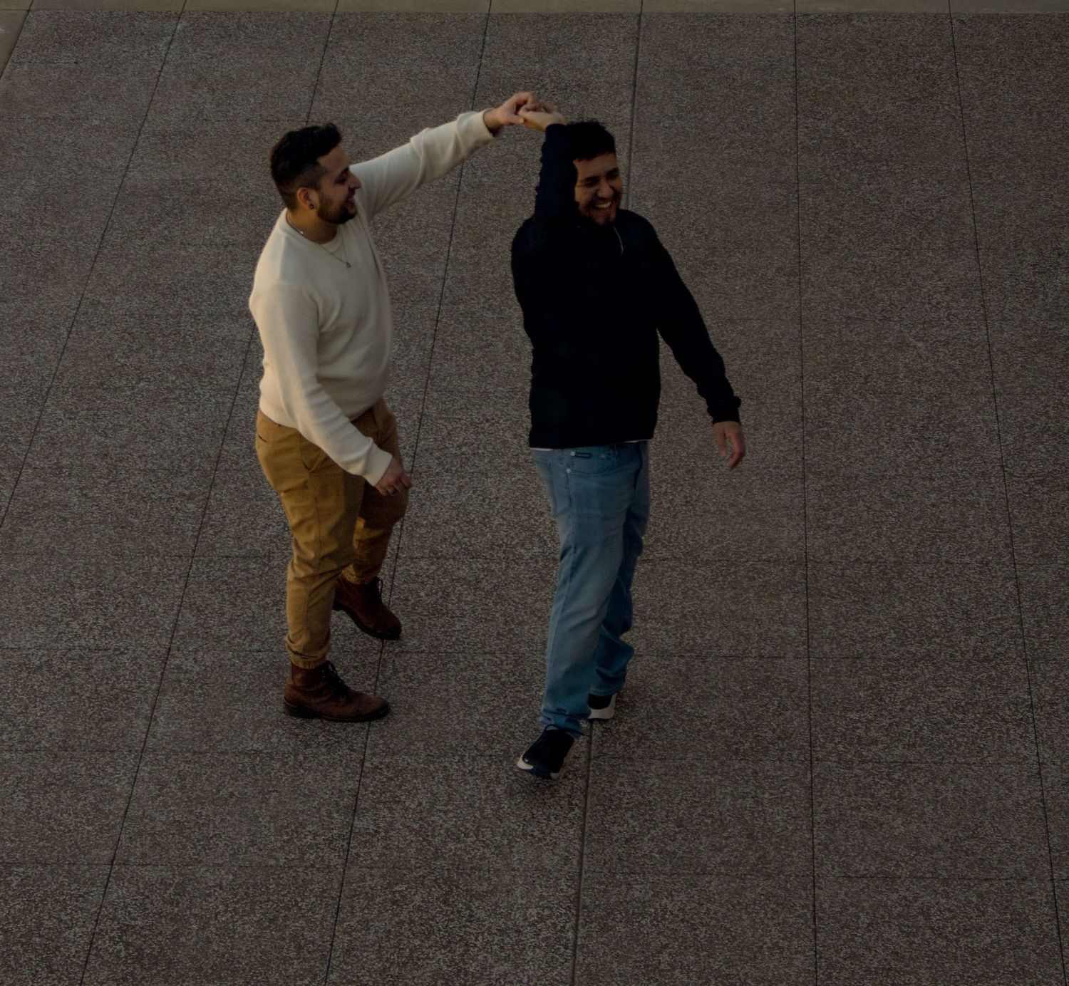 Silhouettes of two people dancing and moving across a grey concrete surface.