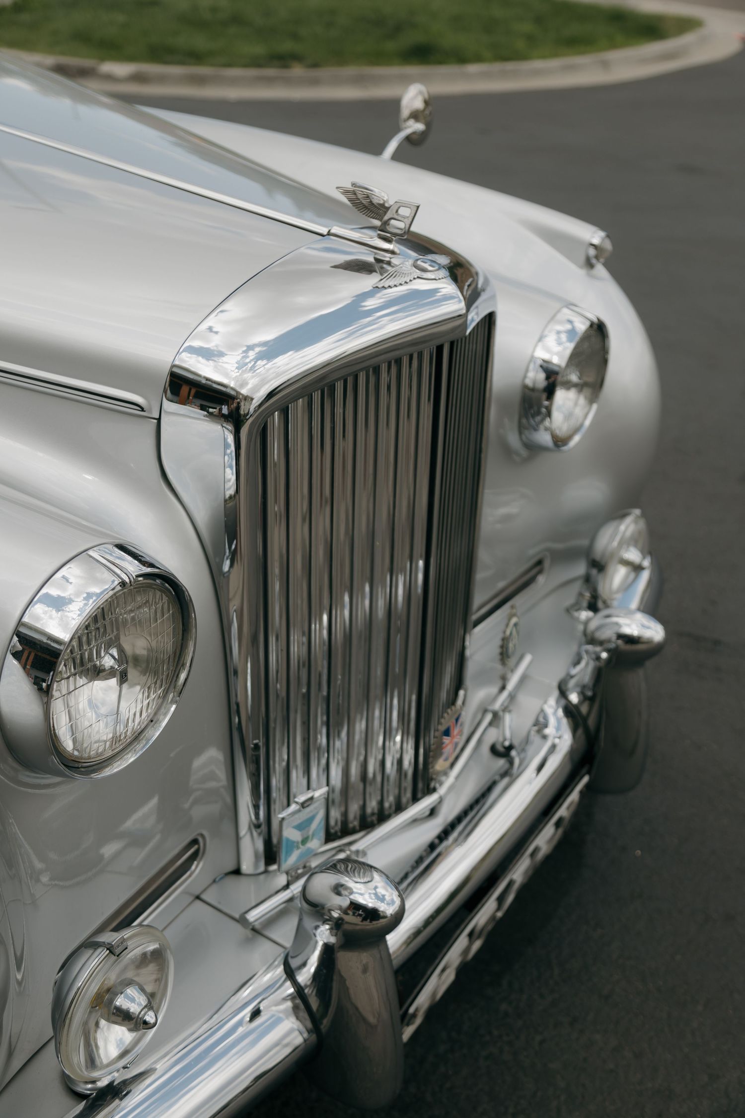 Vintage white Bentley classic car with chrome grille and headlights parked on a driveway.