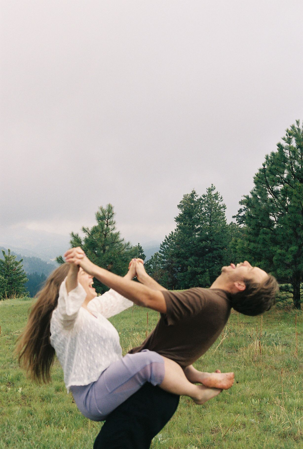 A joyful couple dancing in a meadow, man lifting woman as she leans back with flowing hair, trees behind.