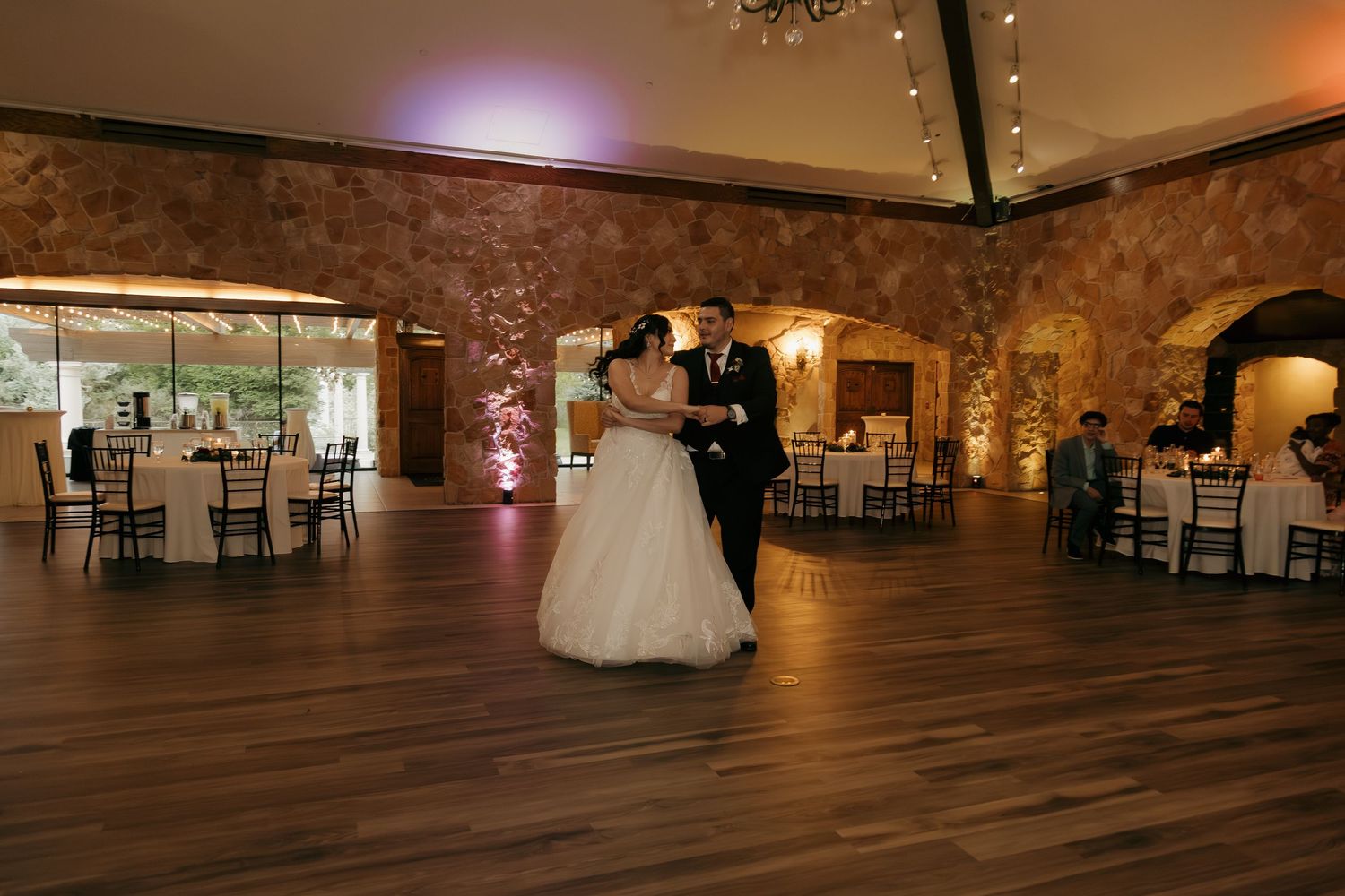 Bride and groom share their first dance in an elegant stone-walled wedding venue with warm amber lighting.