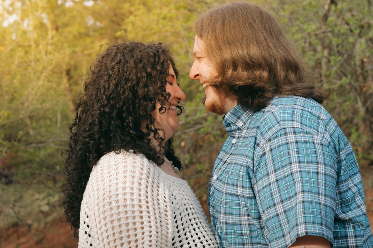 A romantic couple sharing an intimate moment outdoors during golden hour while wearing casual attire.