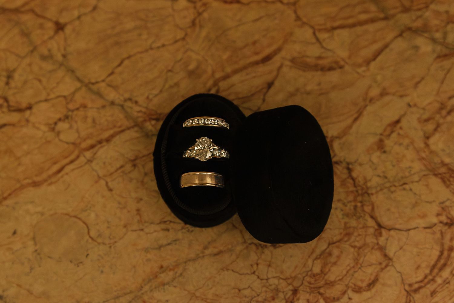 Wedding rings and accessories arranged on textured brown marble surface.
