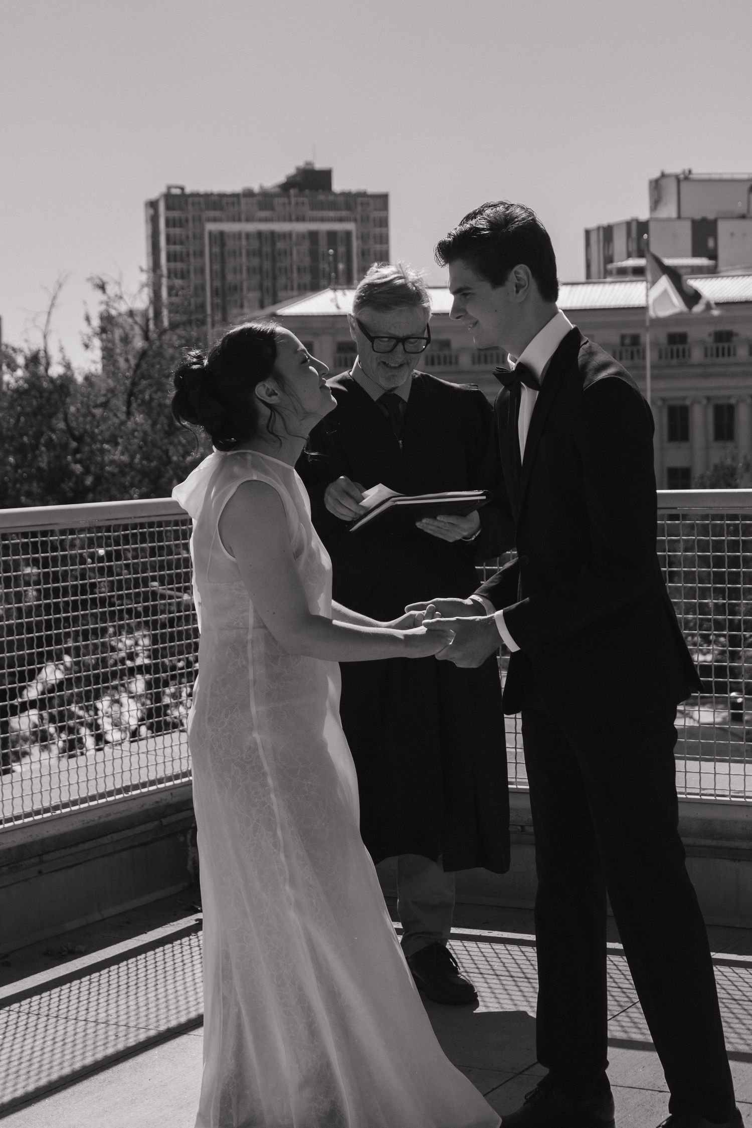 A wedding ceremony taking place on an outdoor terrace with city buildings in the background.