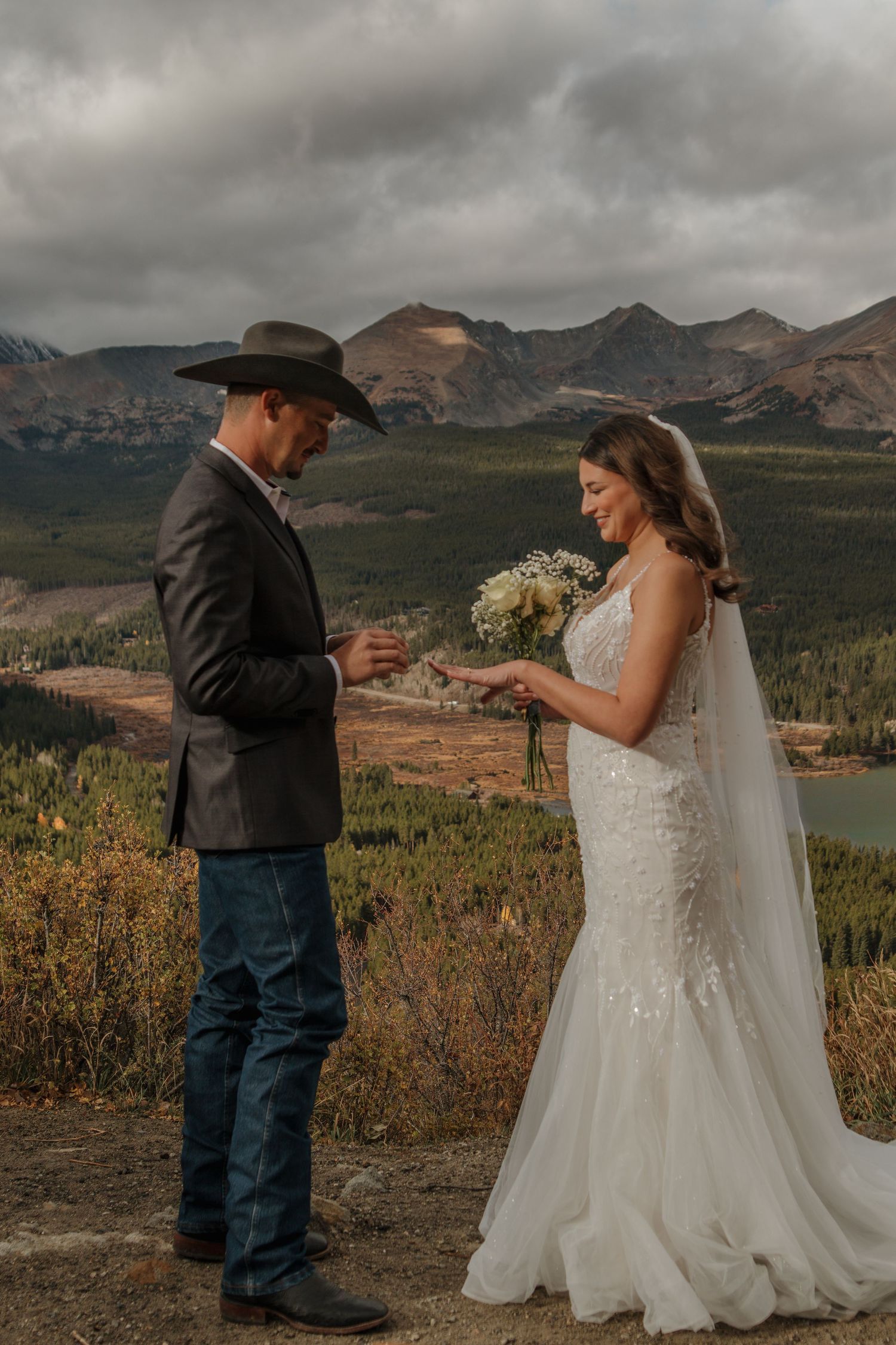 A wedding couple exchanges rings during their ceremony with majestic mountain views in the background.