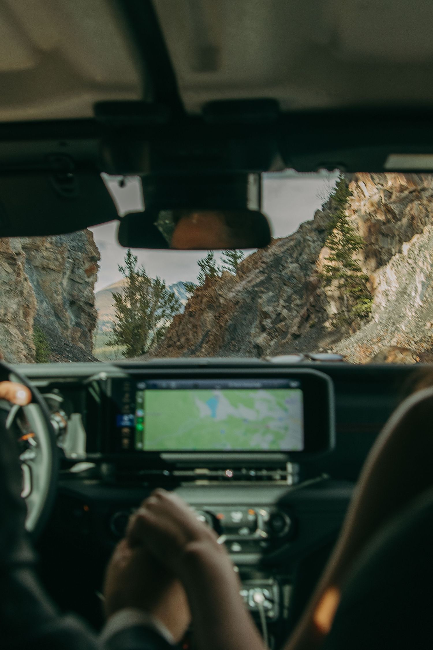 View through car windshield of rocky mountain landscape with navigation system visible.