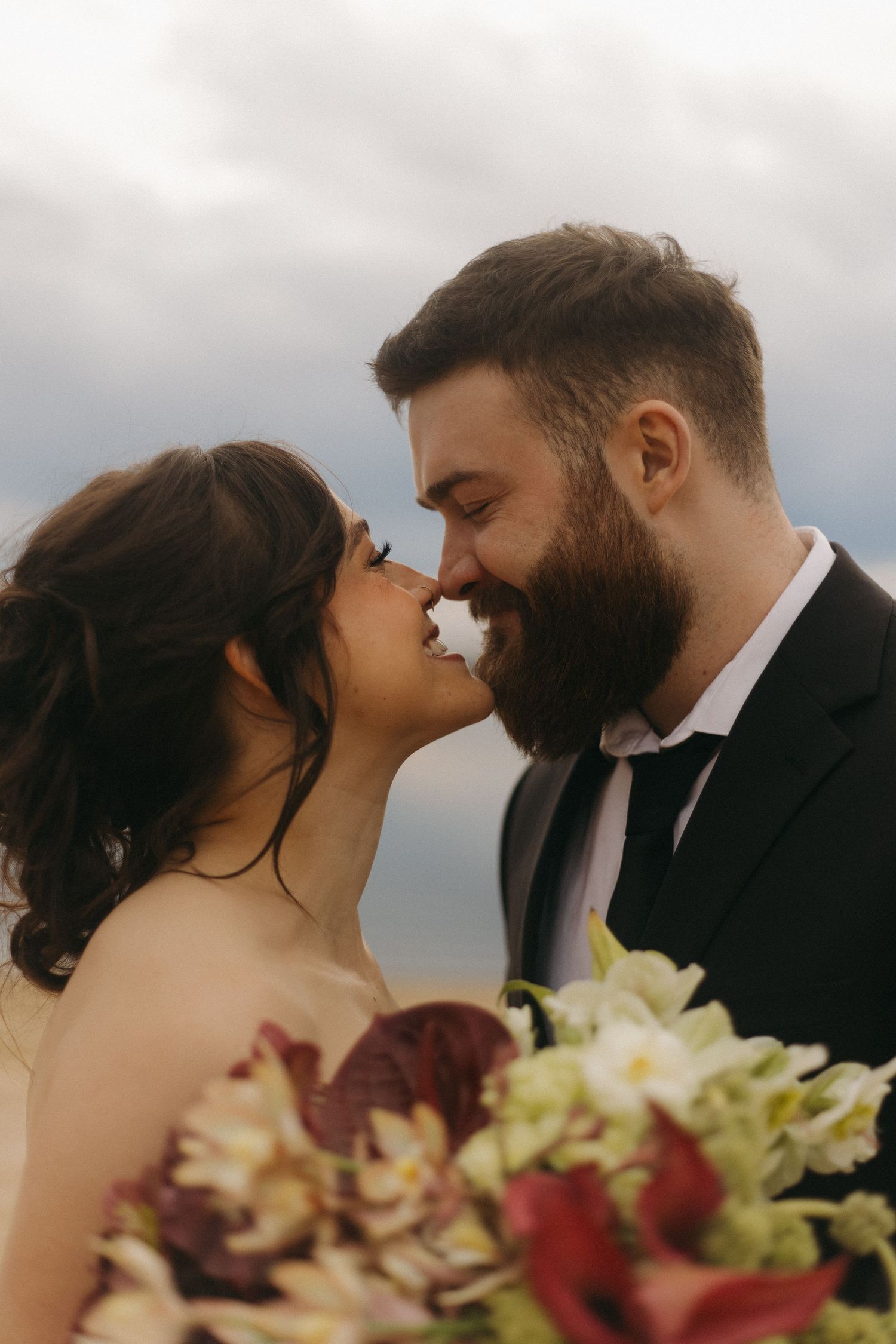 Romantic wedding moment with flowers in the foreground against cloudy sky.
