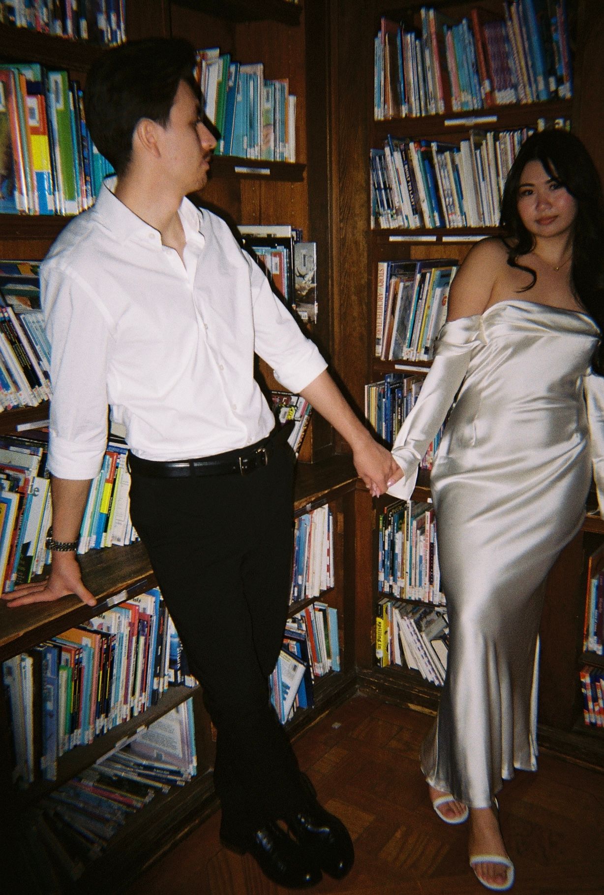Stylish couple in contrasting white and black outfits pose in library setting.