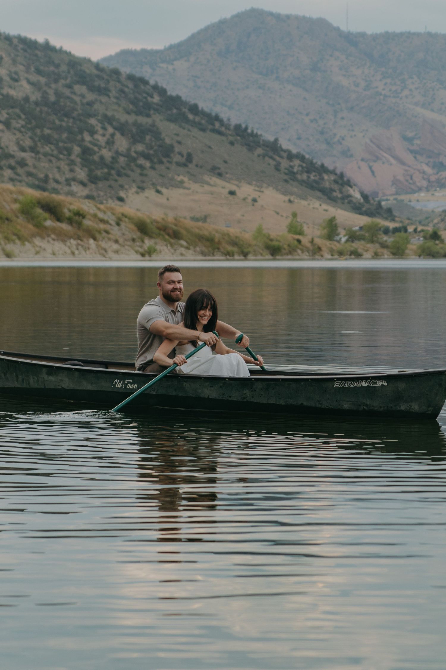 A couple enjoys a serene canoe ride on a lake surrounded by mountain views.