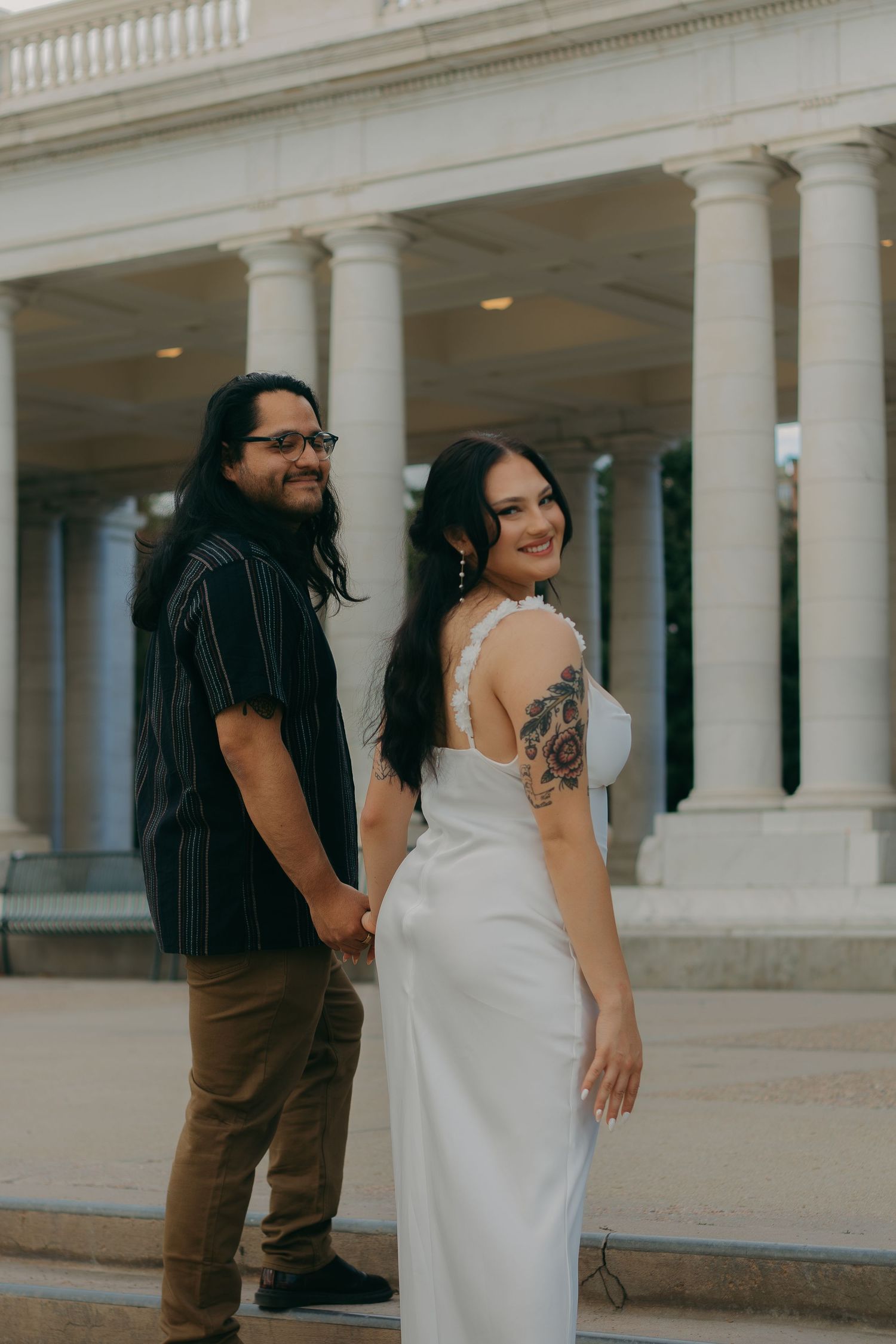 Couple in wedding attire posing together in front of classical white columns.