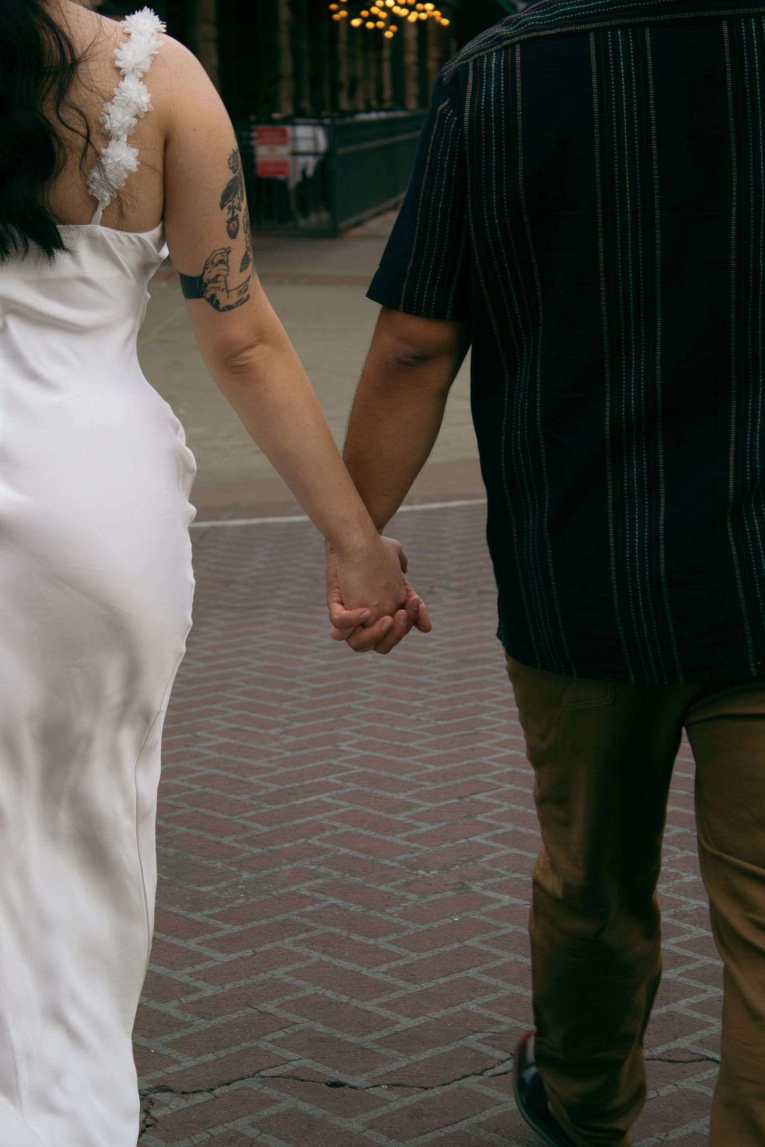 A couple holding hands wearing contrasting white and black outfits on a brick paved walkway.