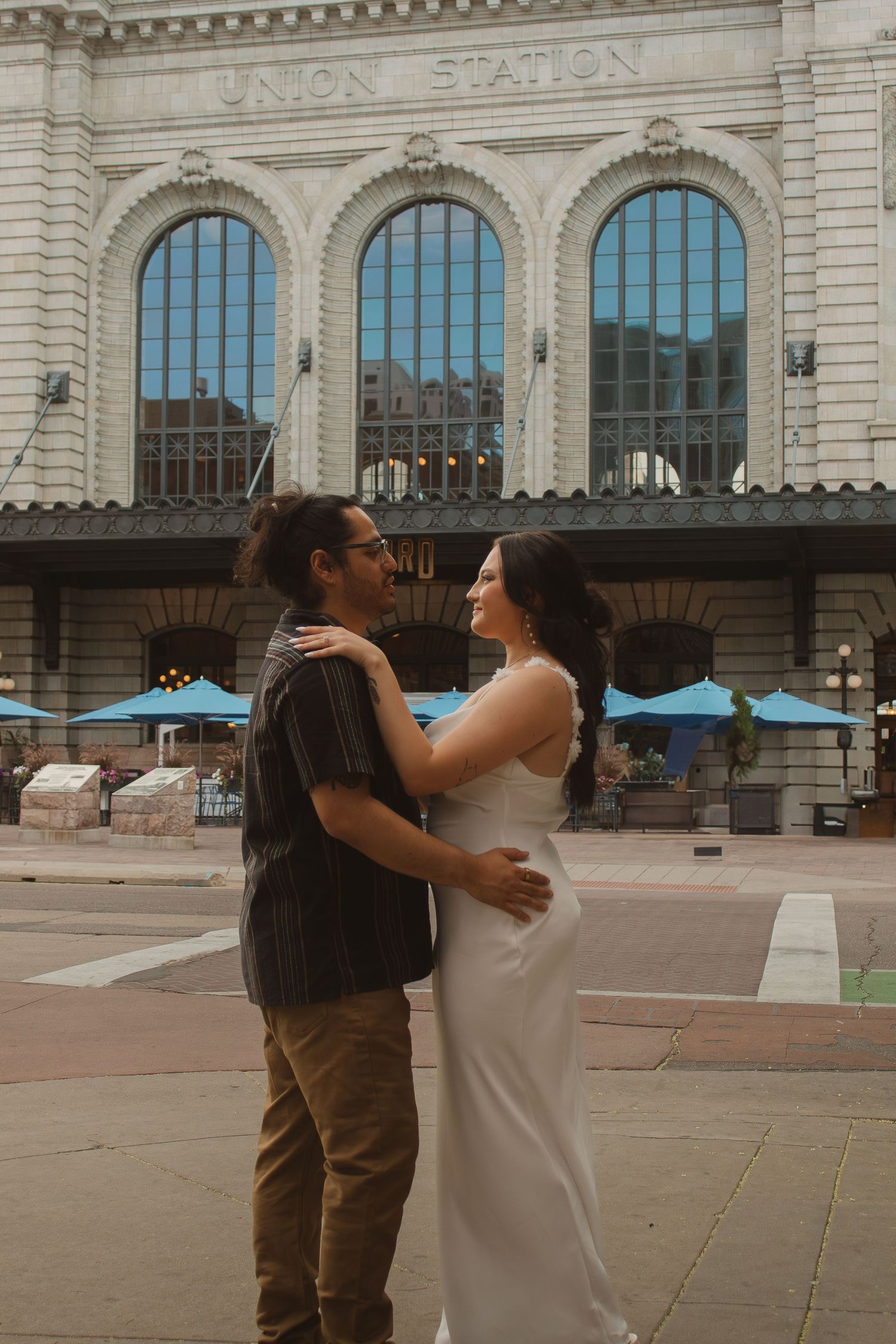 A couple embraces outside Union Station's grand arched entrance with blue umbrellas in the background.