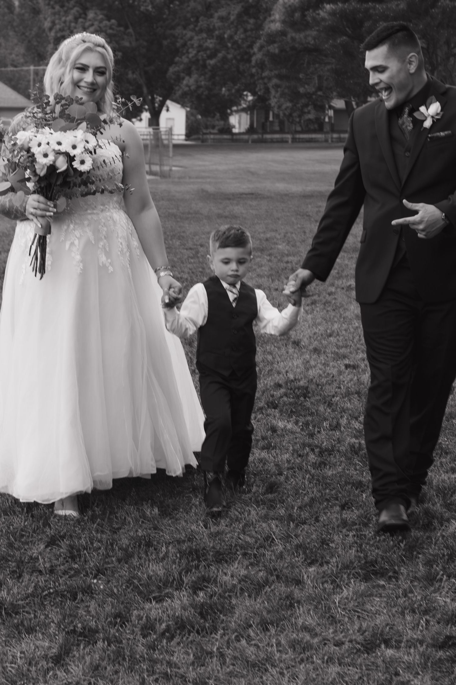 Black and white wedding photo showing tender moment with small ring bearer on lawn.