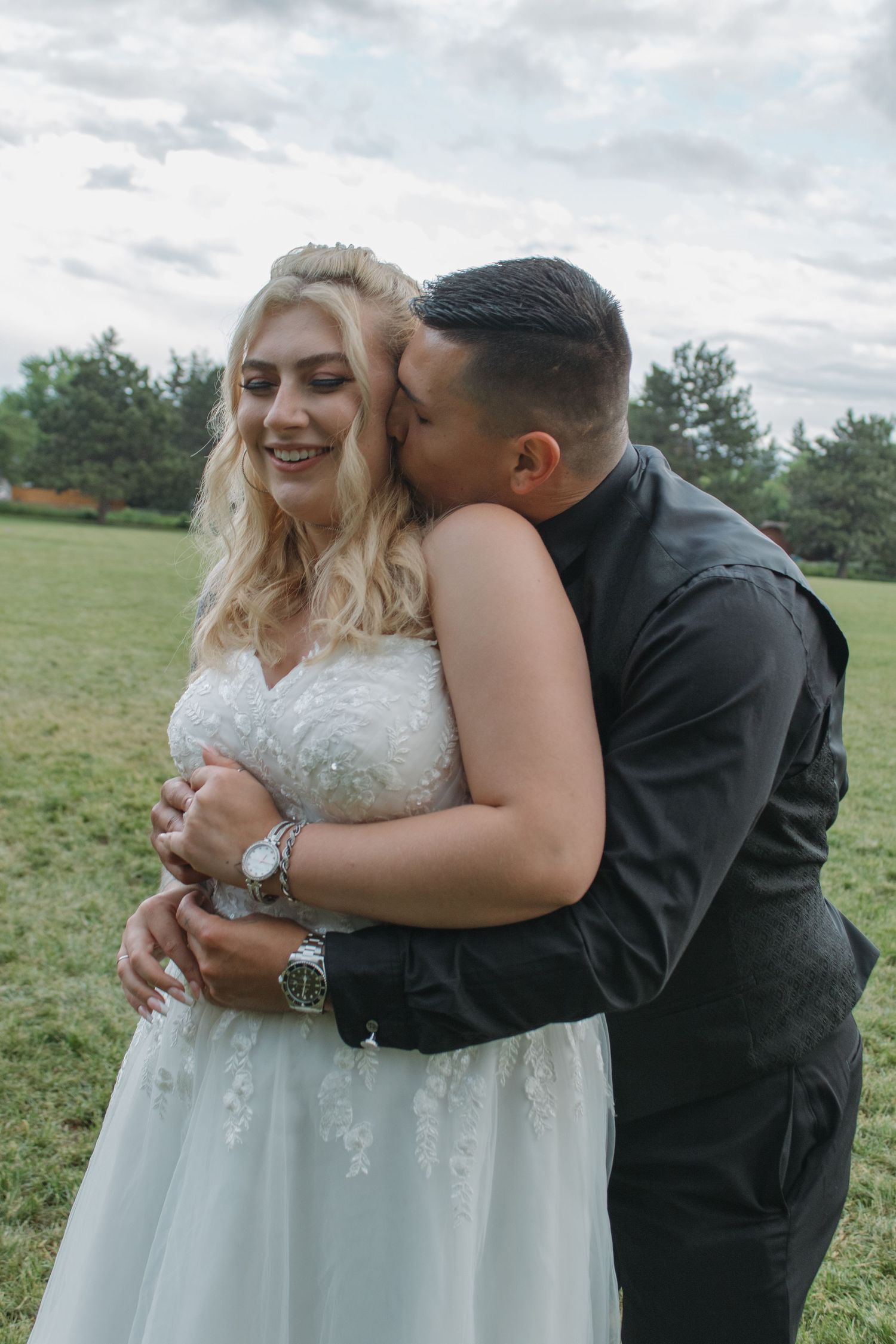Tender moment between newlyweds sharing embraces and laughter in an outdoor setting.