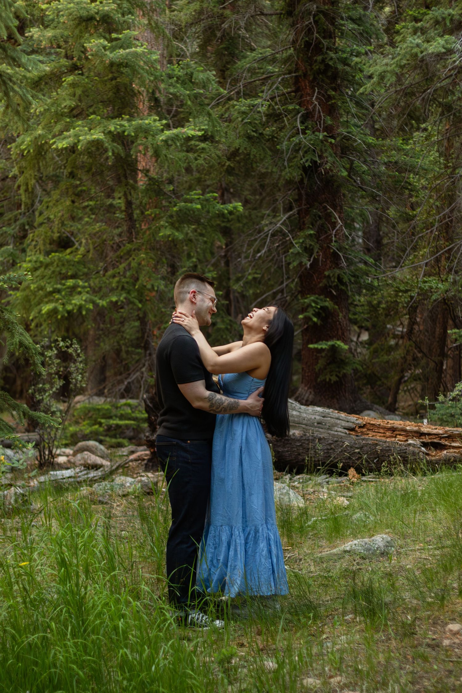 A couple shares a romantic moment in a sunlit forest clearing with evergreen trees.