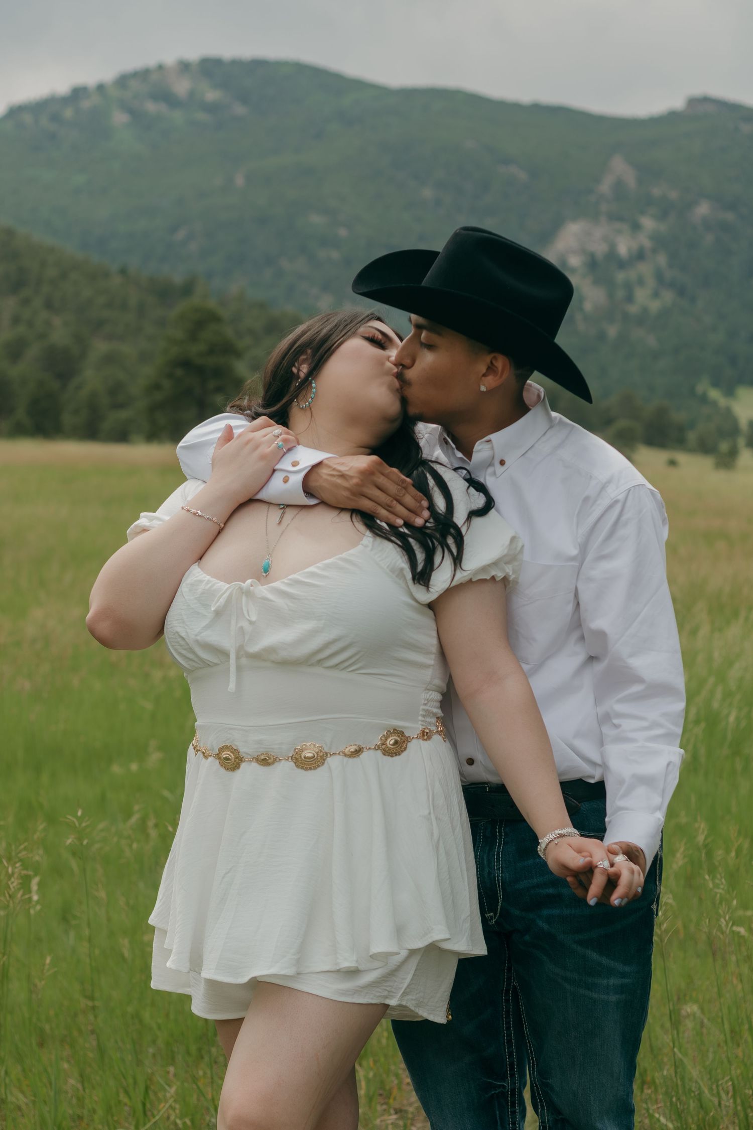 A romantic photo sequence in a mountain field with western attire and natural lighting.