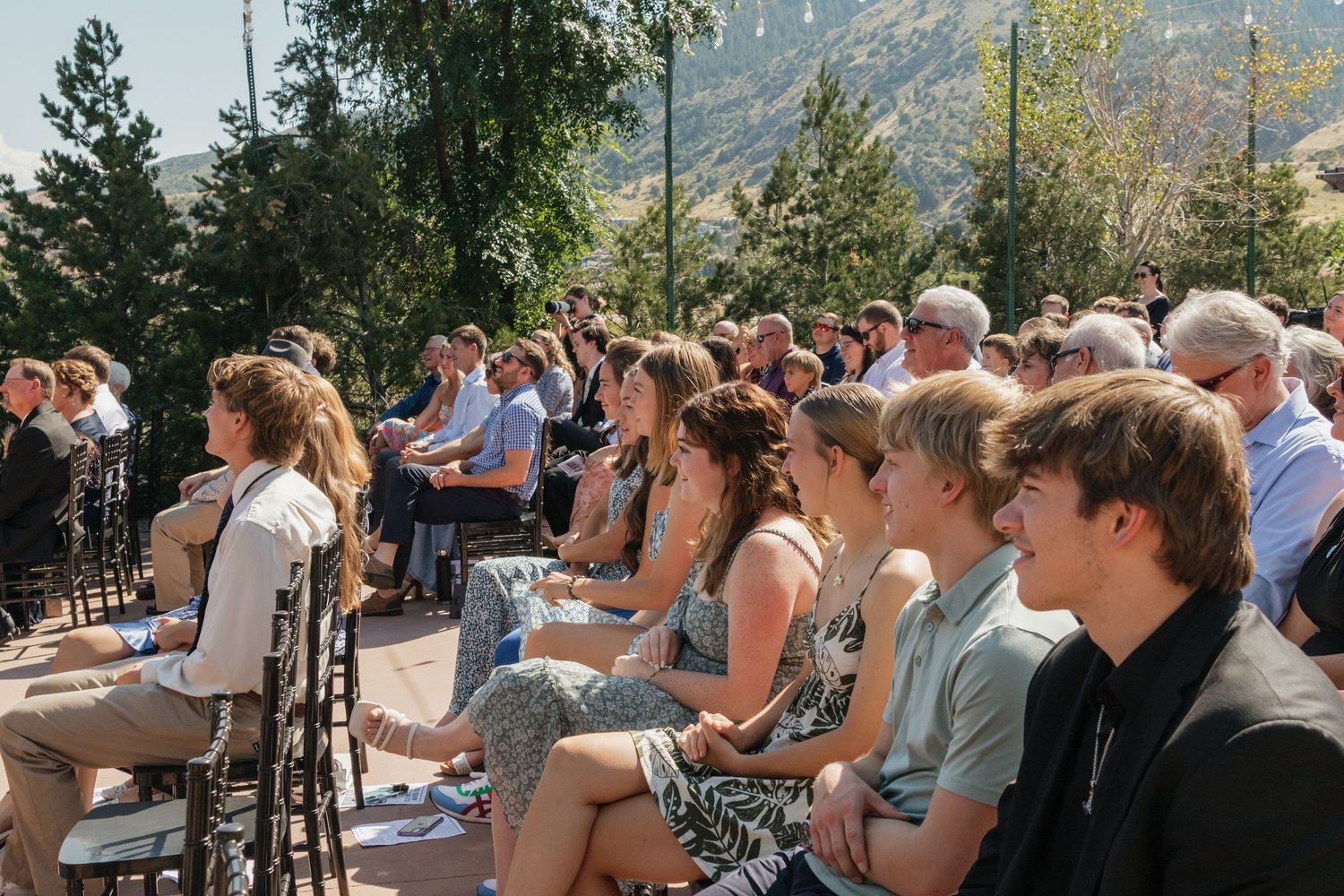 Wedding guests gathered outdoors with mountains visible in the background.