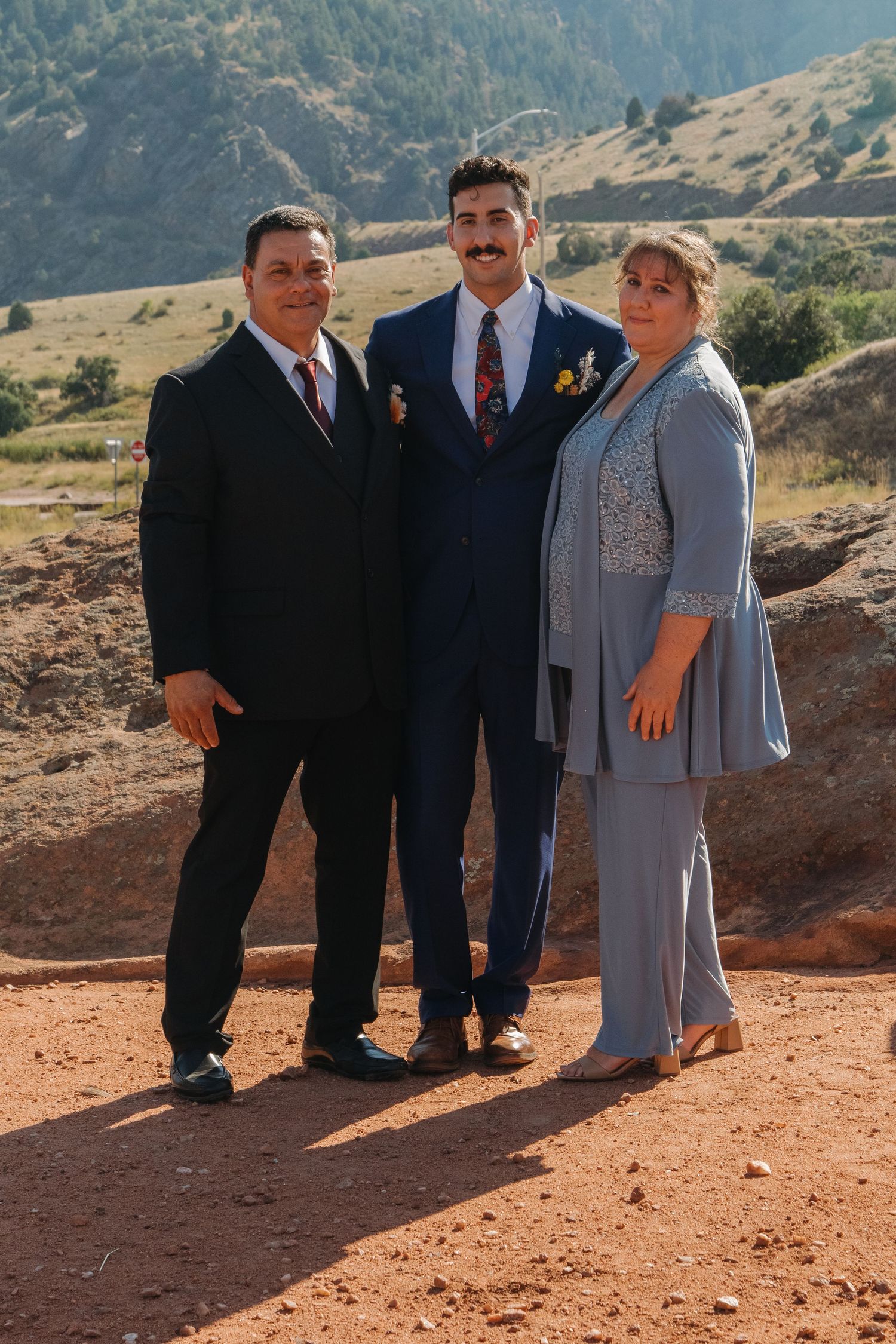 Wedding party members pose for photos on red desert terrain with mountains in the background.