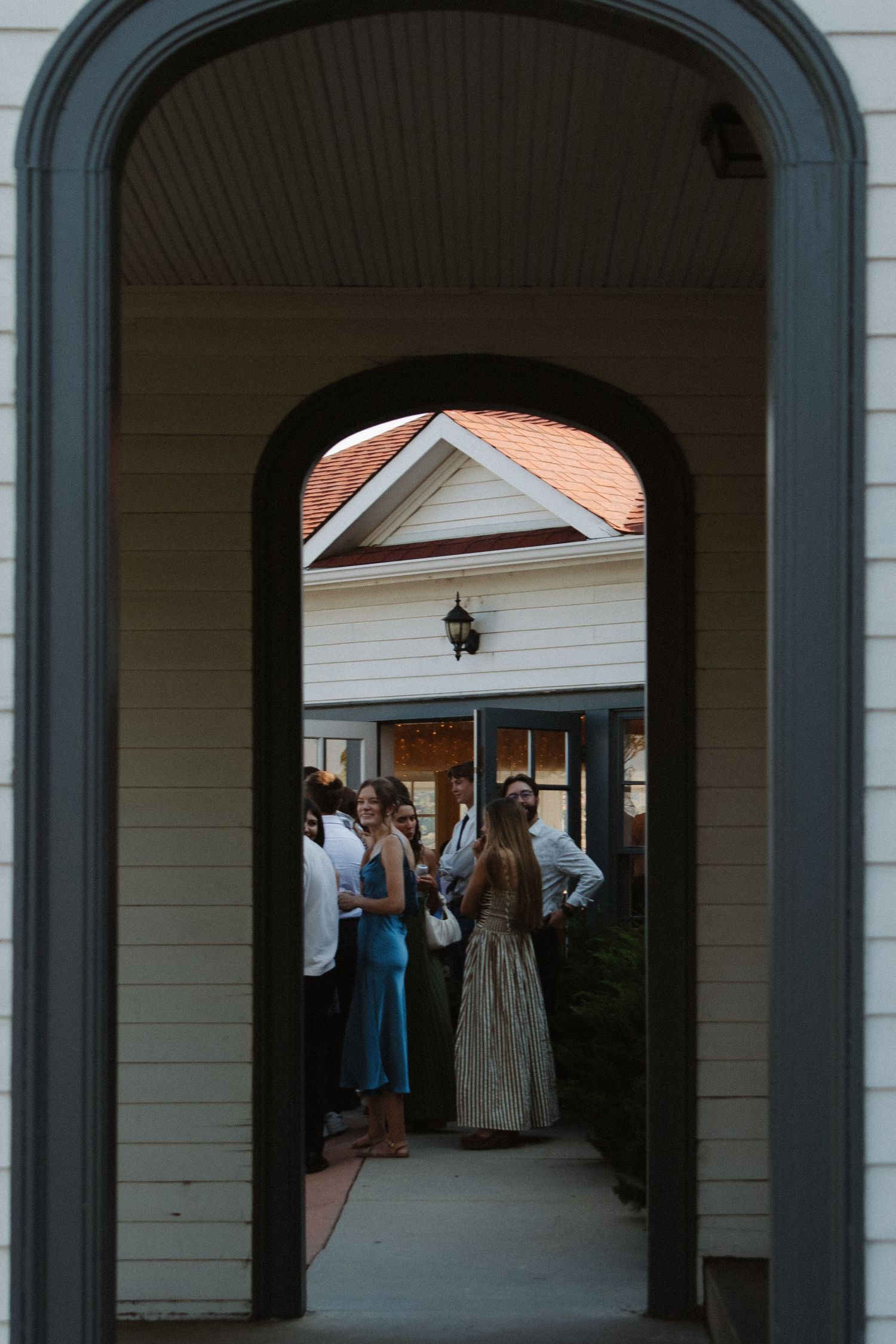 View through arched colonnade showing wedding guests gathering outside.