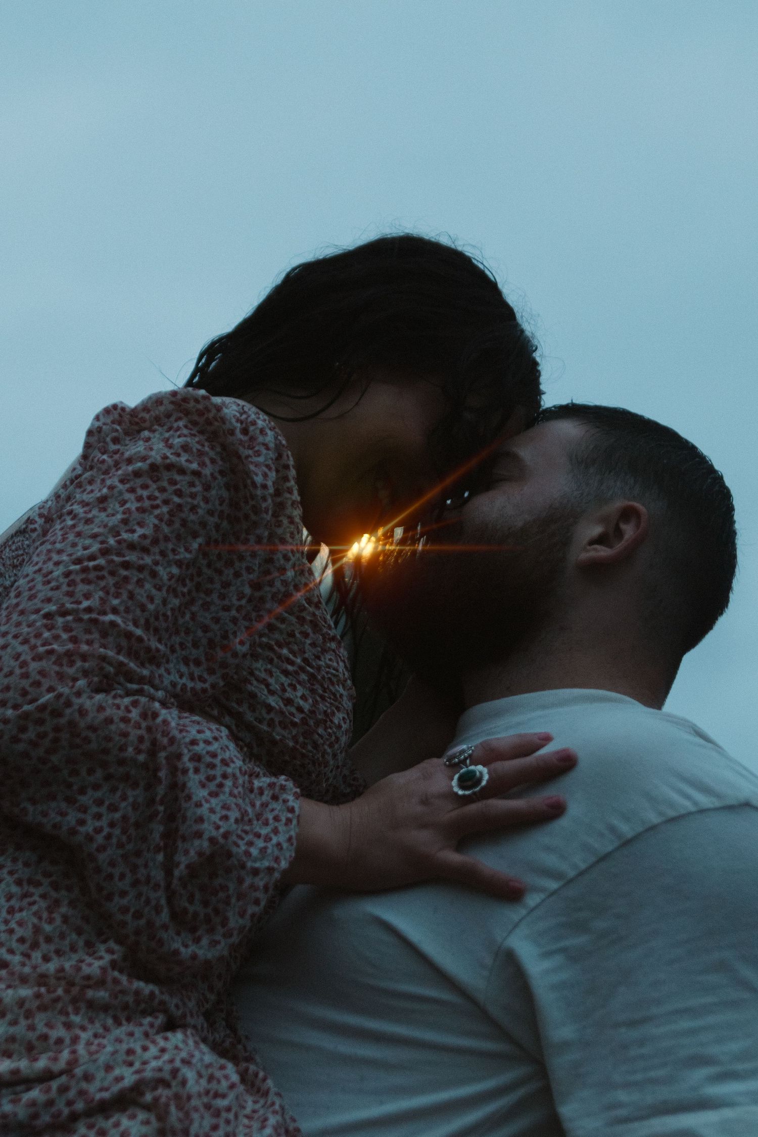 Silhouetted couple sharing an intimate moment at sunset with lens flare in background.