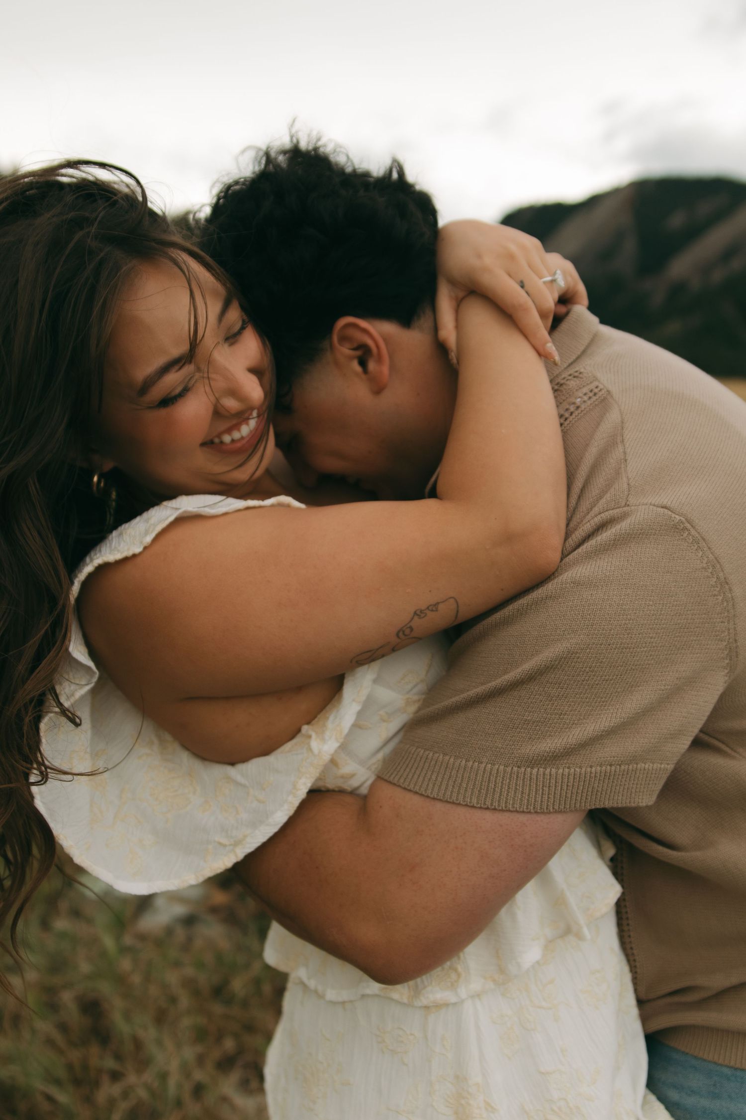 Couple sharing a tender embrace outdoors, woman laughing joyfully in a white dress.