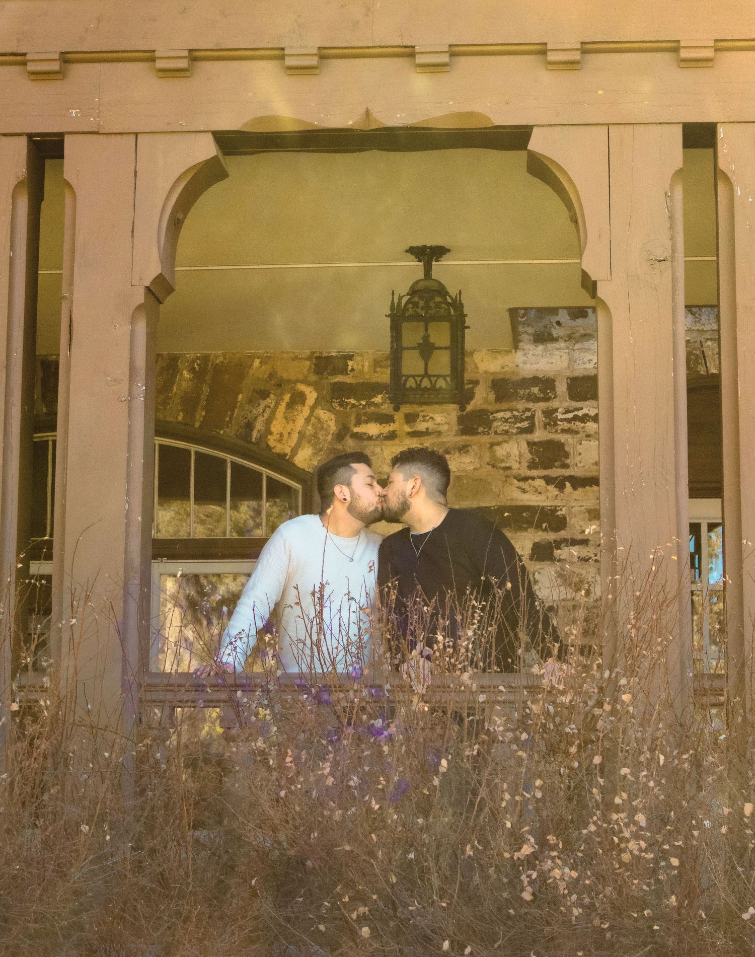 A couple in an intimate pose framed by a vintage archway and dried foliage.