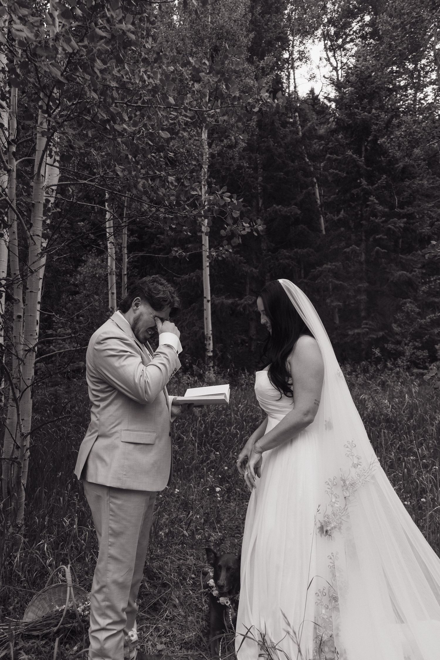 Emotional black and white photo of groom reading vows while bride listens in forest elopement.