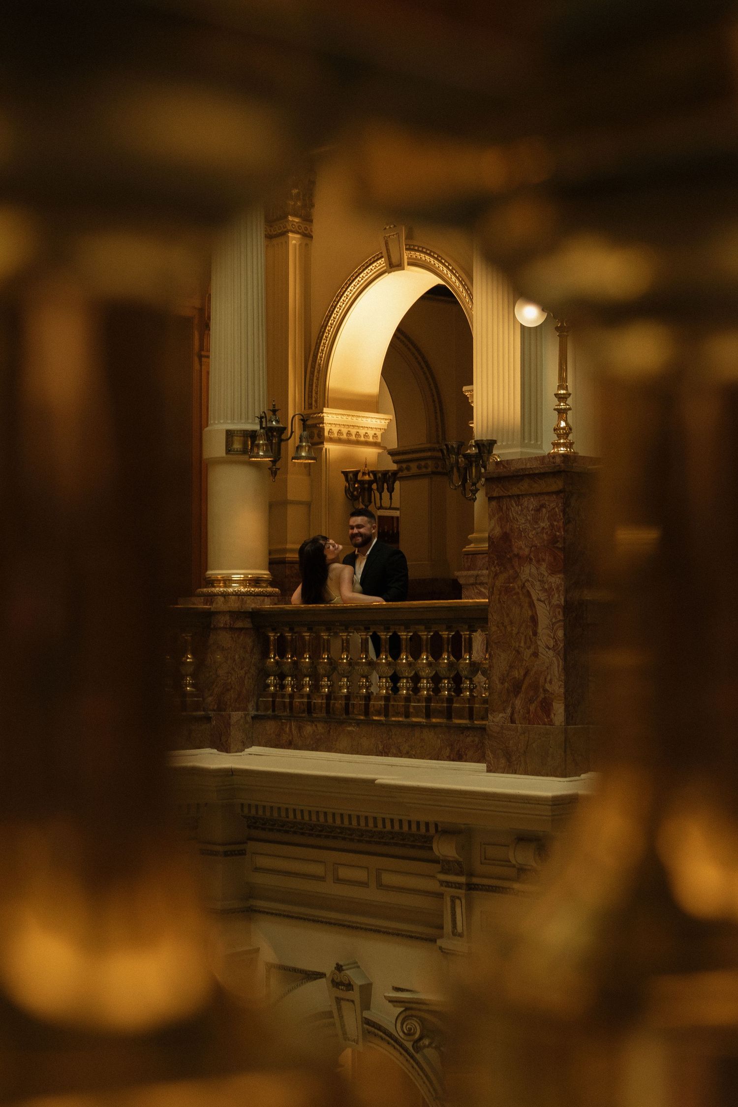 A romantic silhouette of a couple against an ornate archway in a dimly lit historic space.