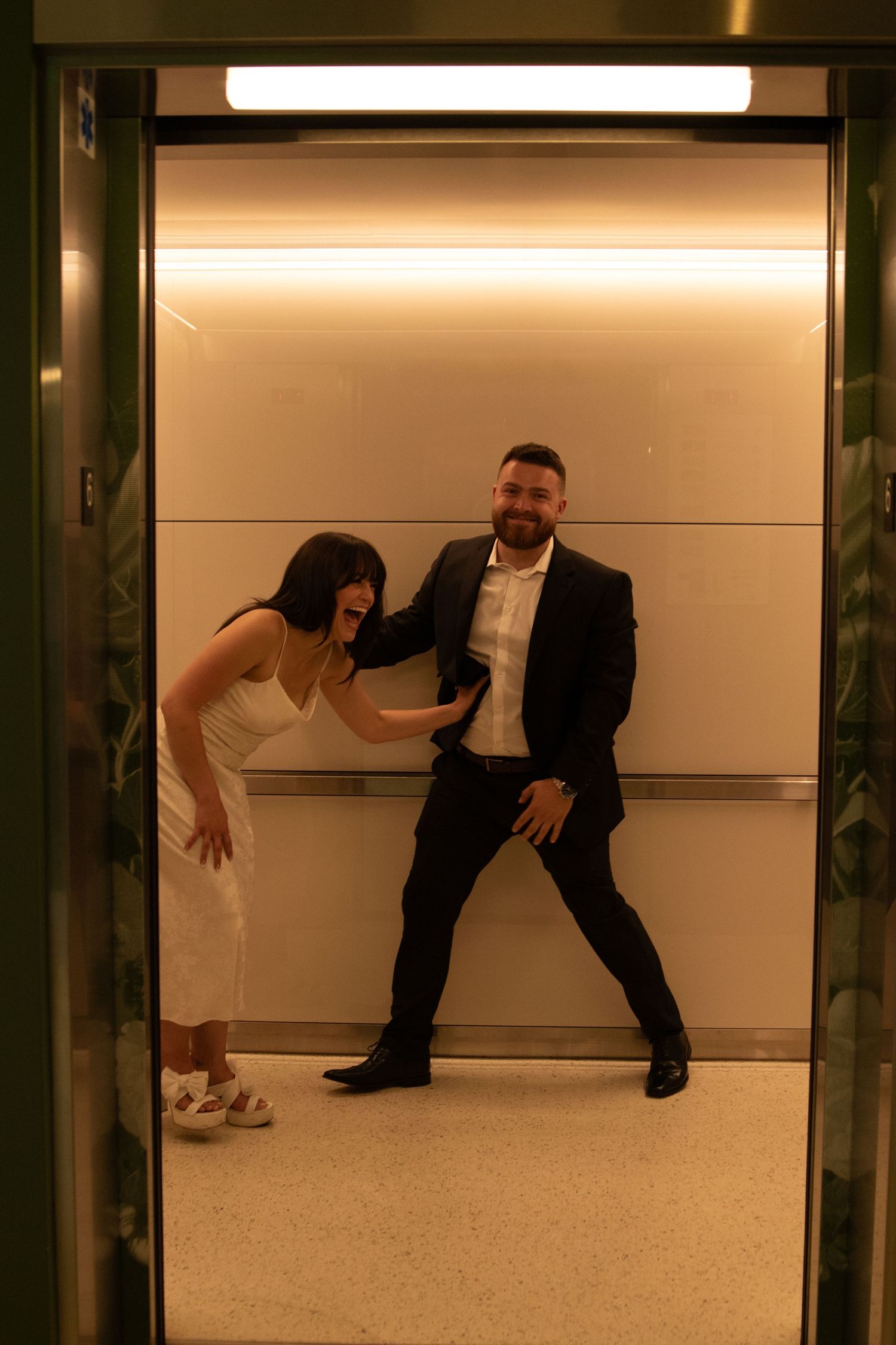 Artistic couple pose in minimalist hallway with warm lighting.