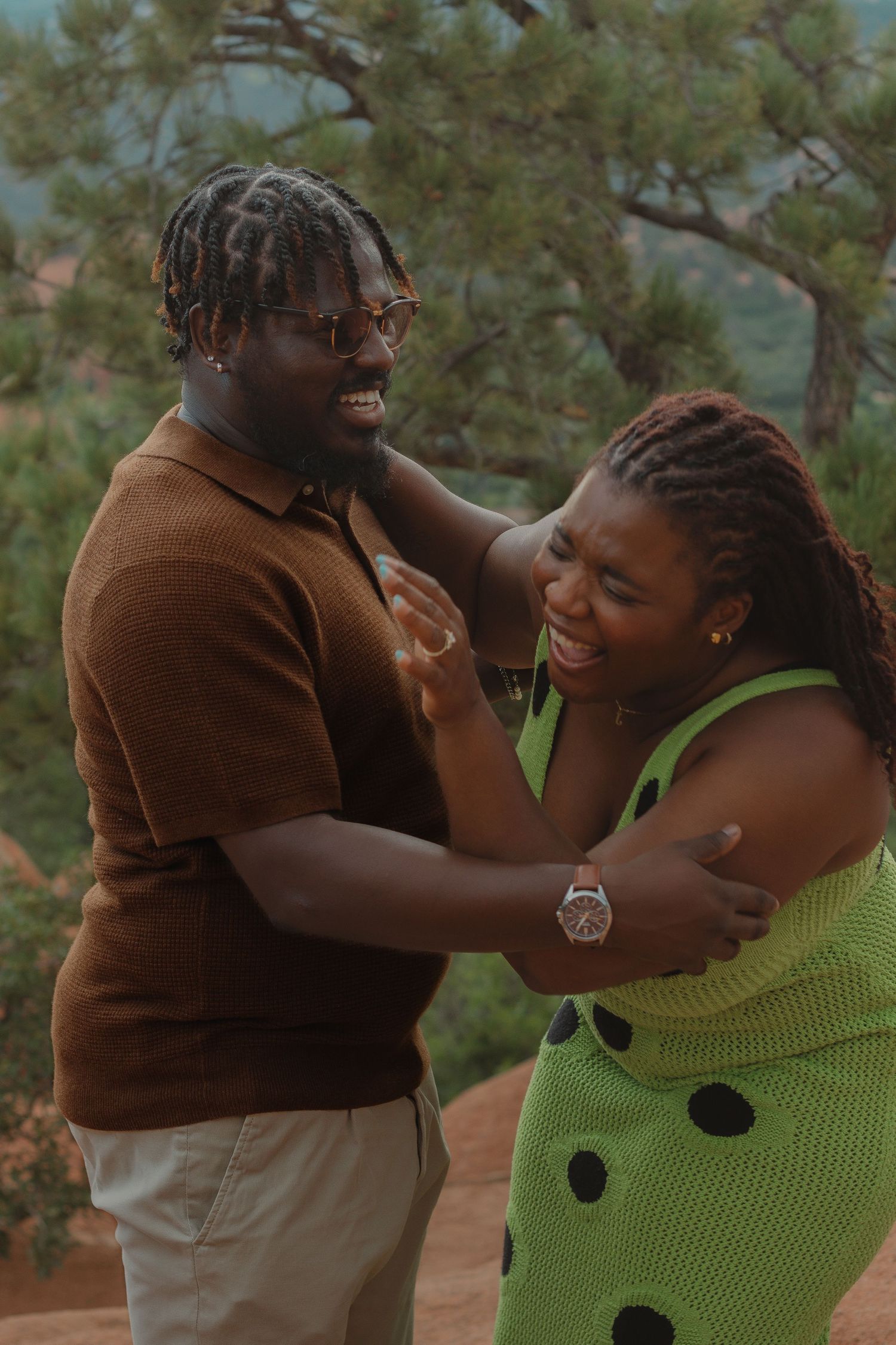 A joyful couple shares a playful moment outdoors, wearing brown and lime green outfits against a natural backdrop.