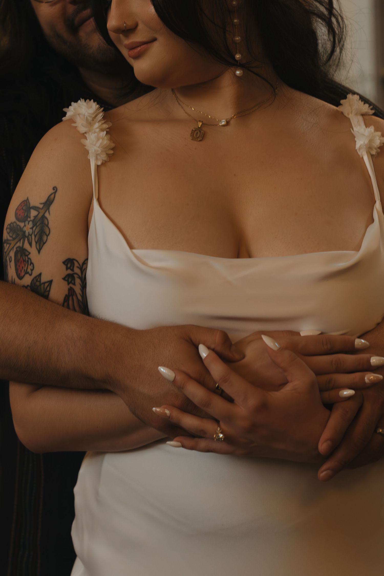 White wedding dress with delicate straps and close embrace showing visible tattoo artwork.