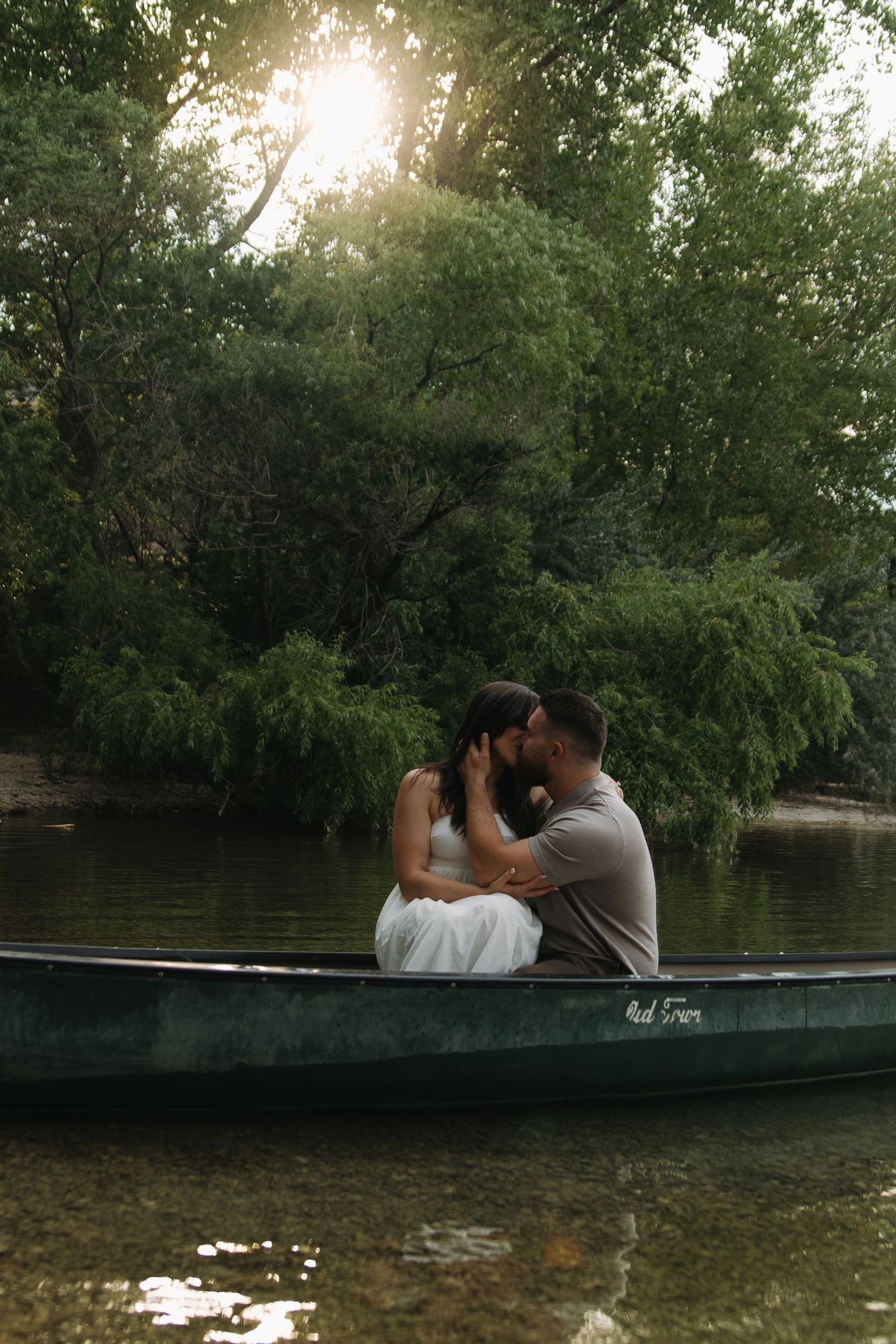 Sunset boat photoshoot with couple against lush green trees.
