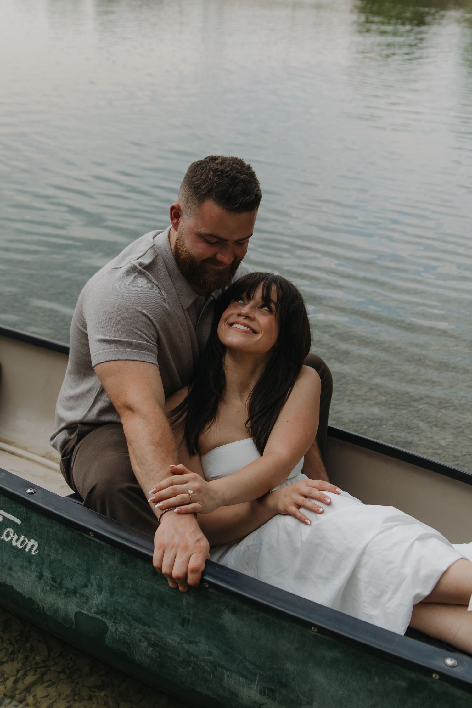 A romantic couple shares intimate moments while lounging in a canoe on a peaceful lake.