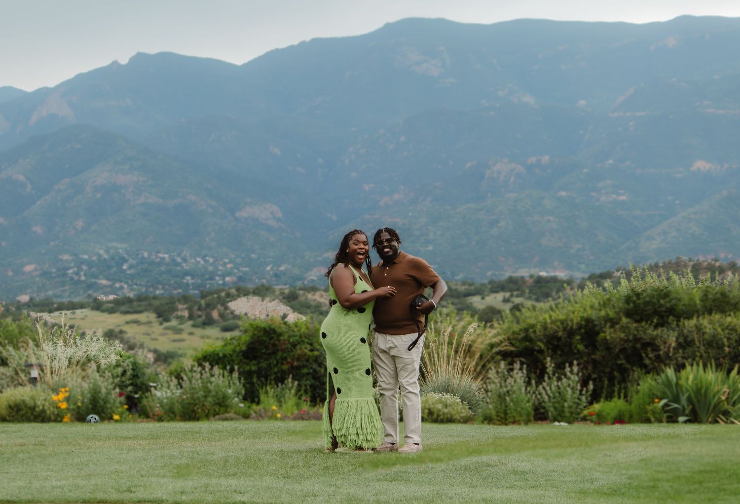 A couple stands together on a lush golf course with scenic mountain views in the background.