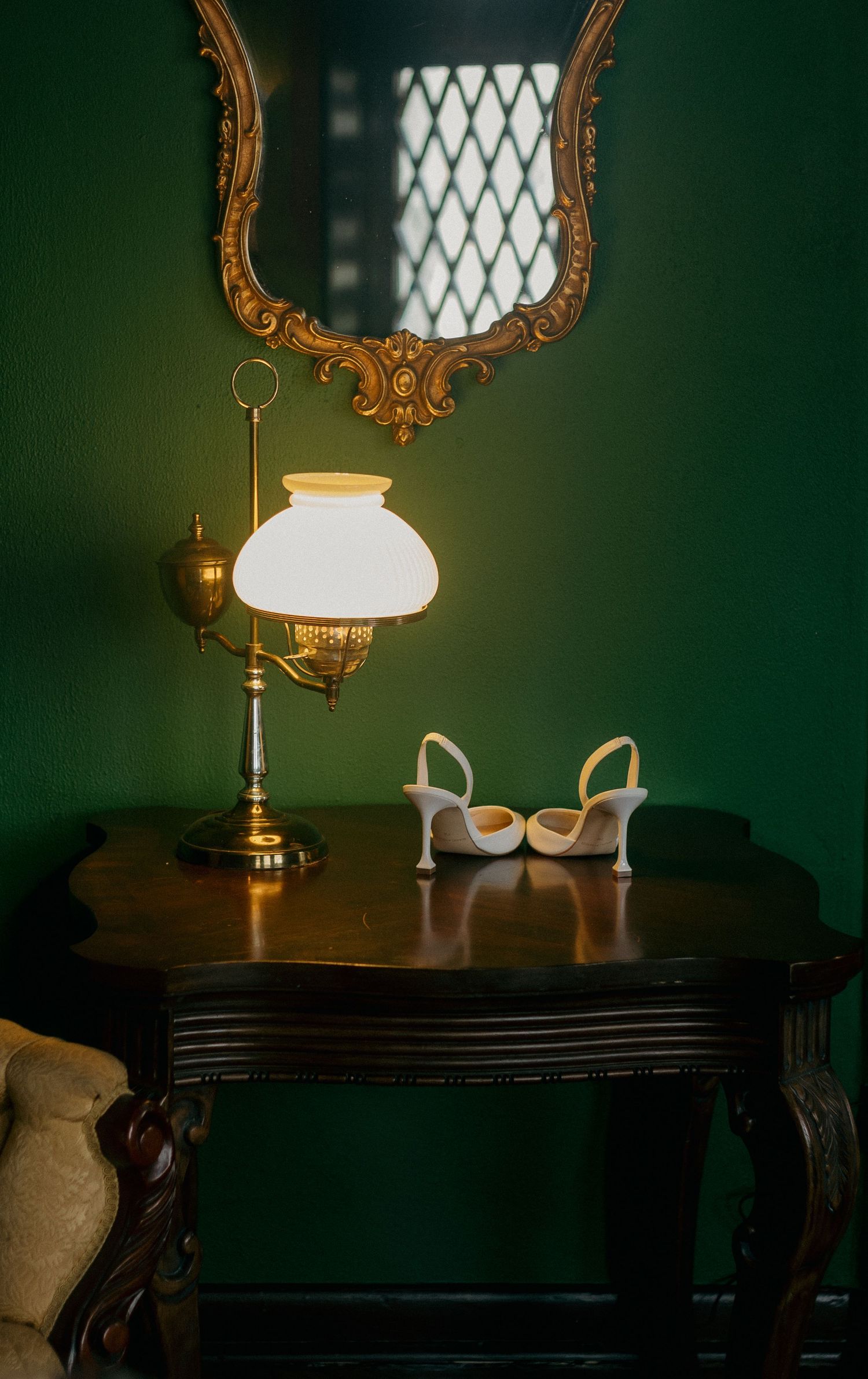 An elegant antique table with ornate mirror and vintage lamp against a deep green wall.