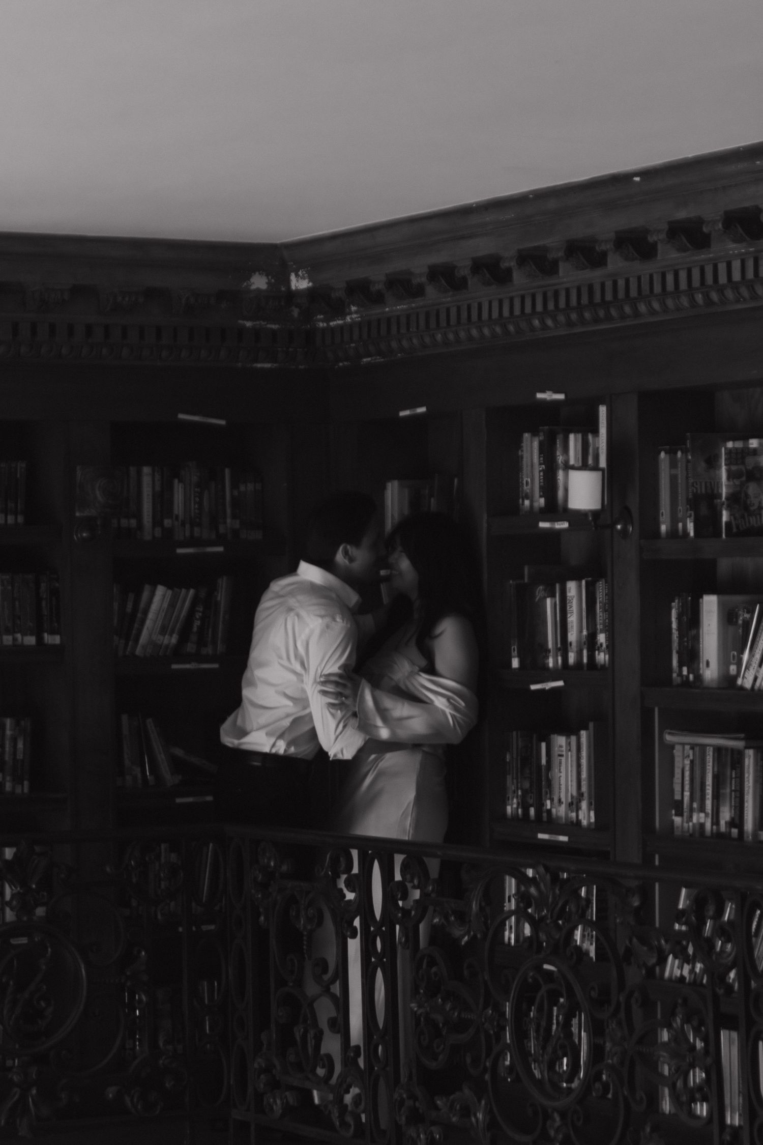 Black and white photo of library shelves with books and someone searching through them.