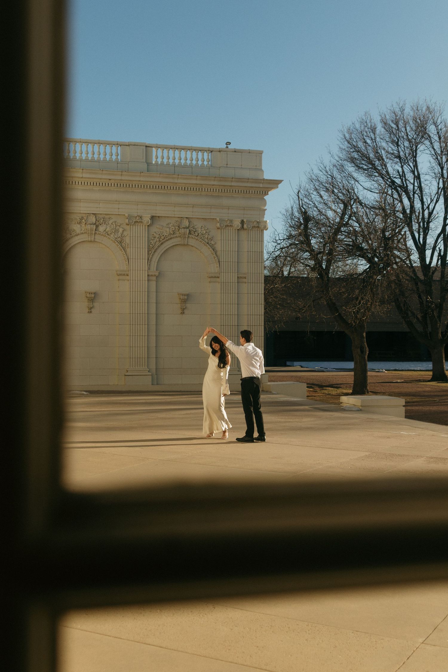 A couple stands near an ornate white stone architectural structure in afternoon light.
