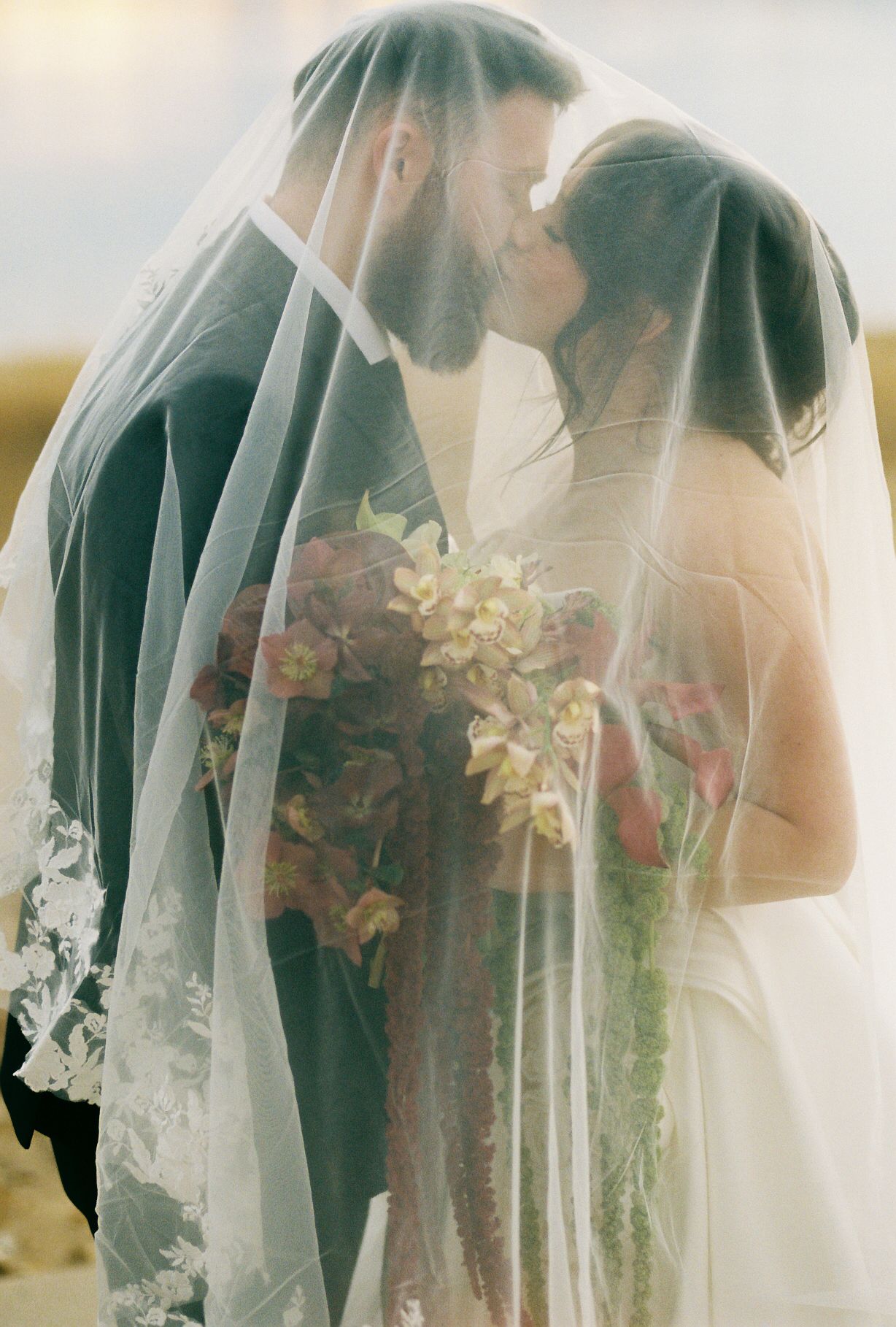 An ethereal wedding portrait through delicate veil fabric with soft golden light filtering through.
