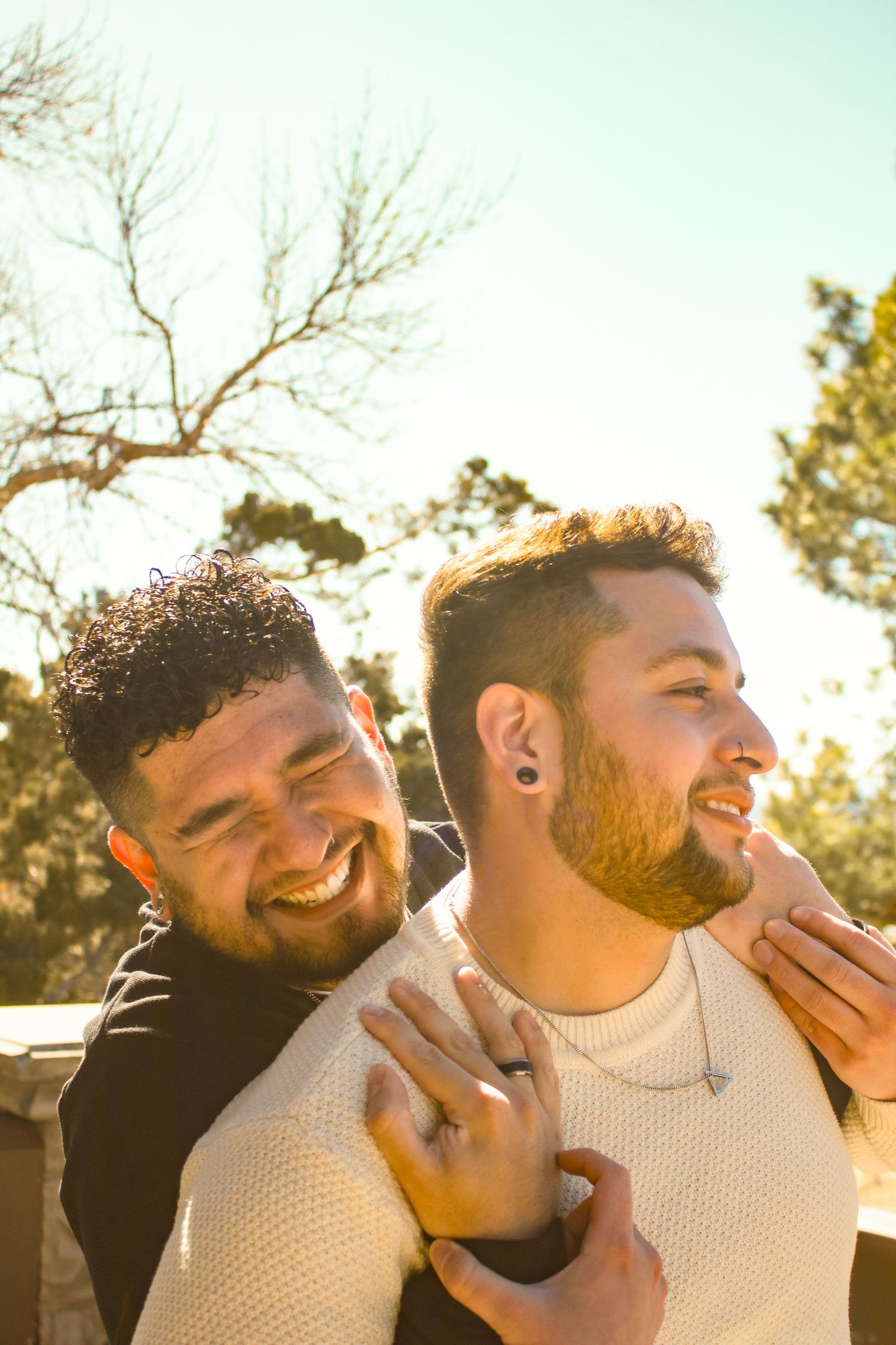 Two people share an intimate moment outdoors during sunset with pine trees in the background.