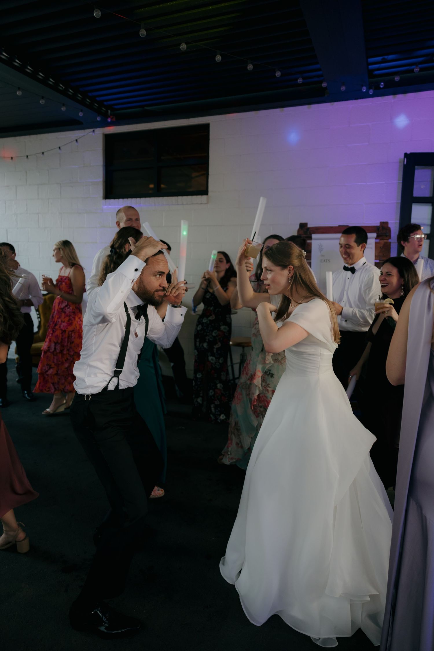 Bride and groom dancing with glow sticks surrounded by guests at wedding reception.