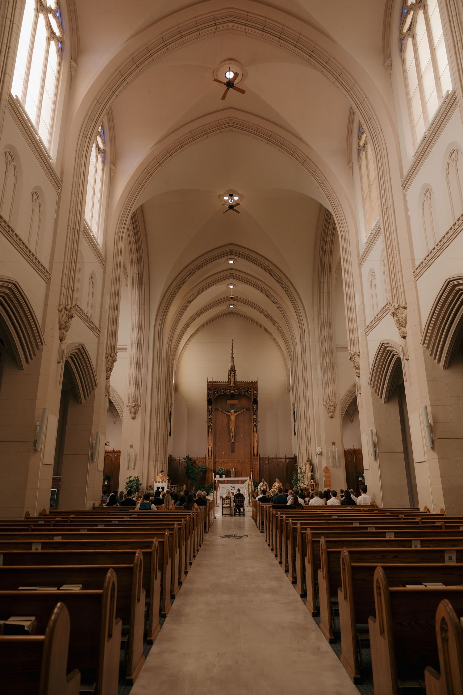 Grand Gothic Catholic church interior with vaulted arches, wooden pews, and crucifix at altar.