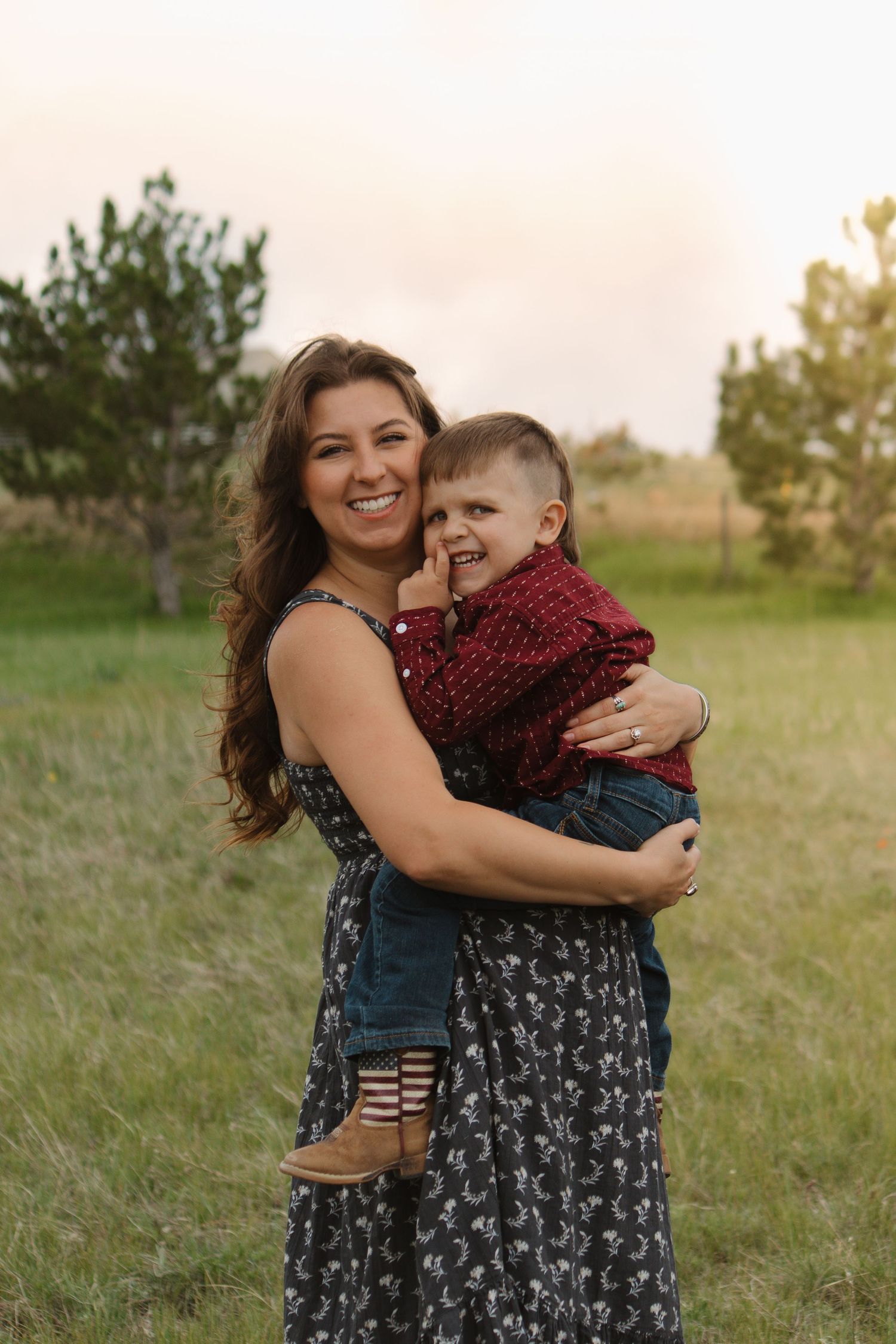 A joyful moment captured outdoors in a floral dress against a natural sunset backdrop.