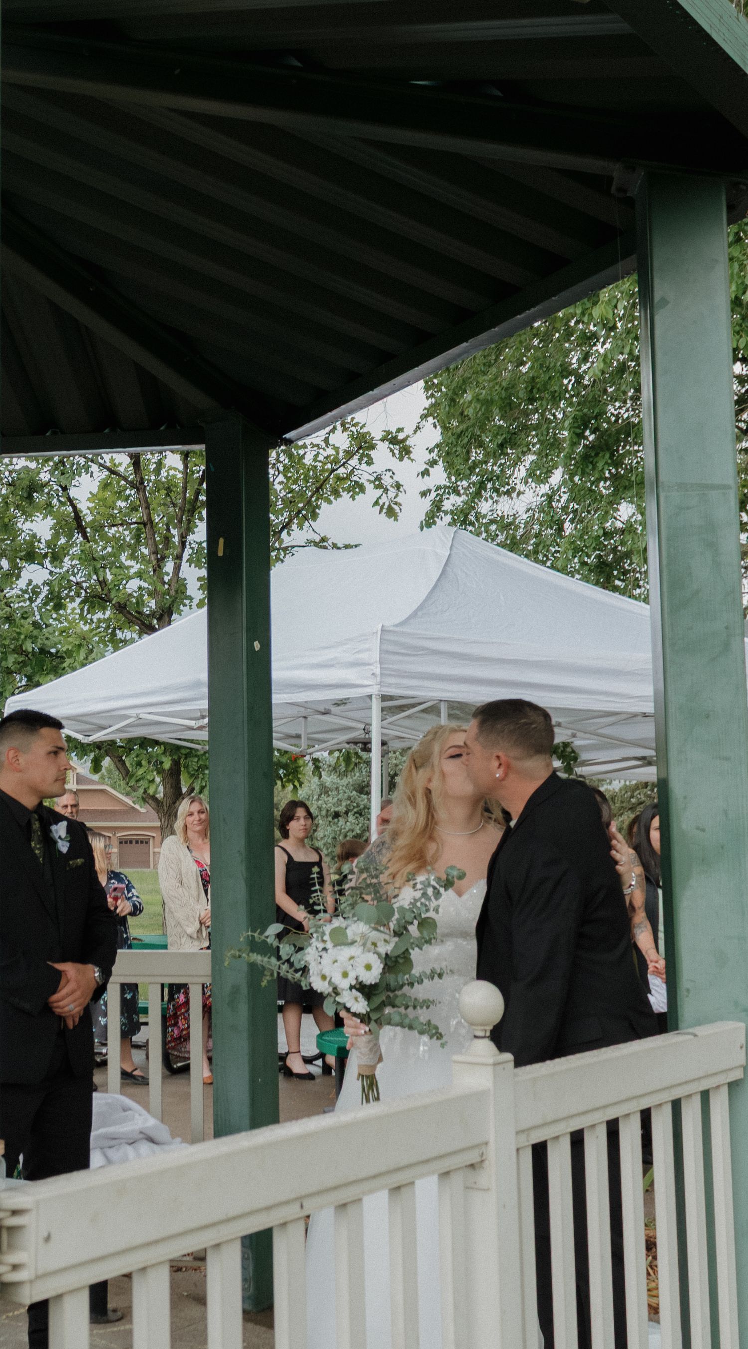 Wedding ceremony participants gathered under white gazebo during outdoor celebration.